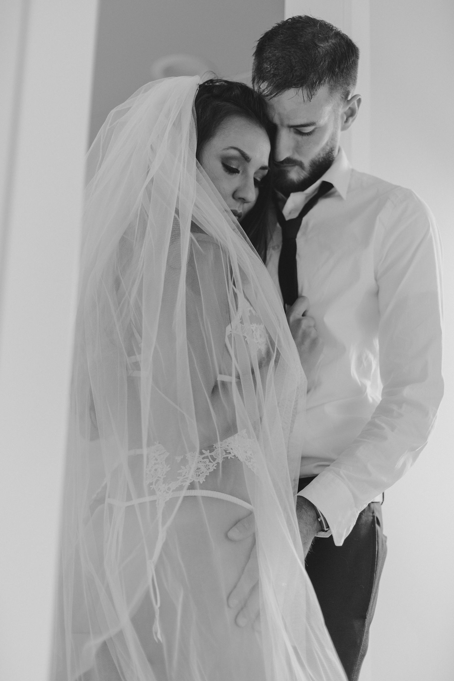 Monochrome intimate wedding photo of couple in formal attire sharing tender moment.