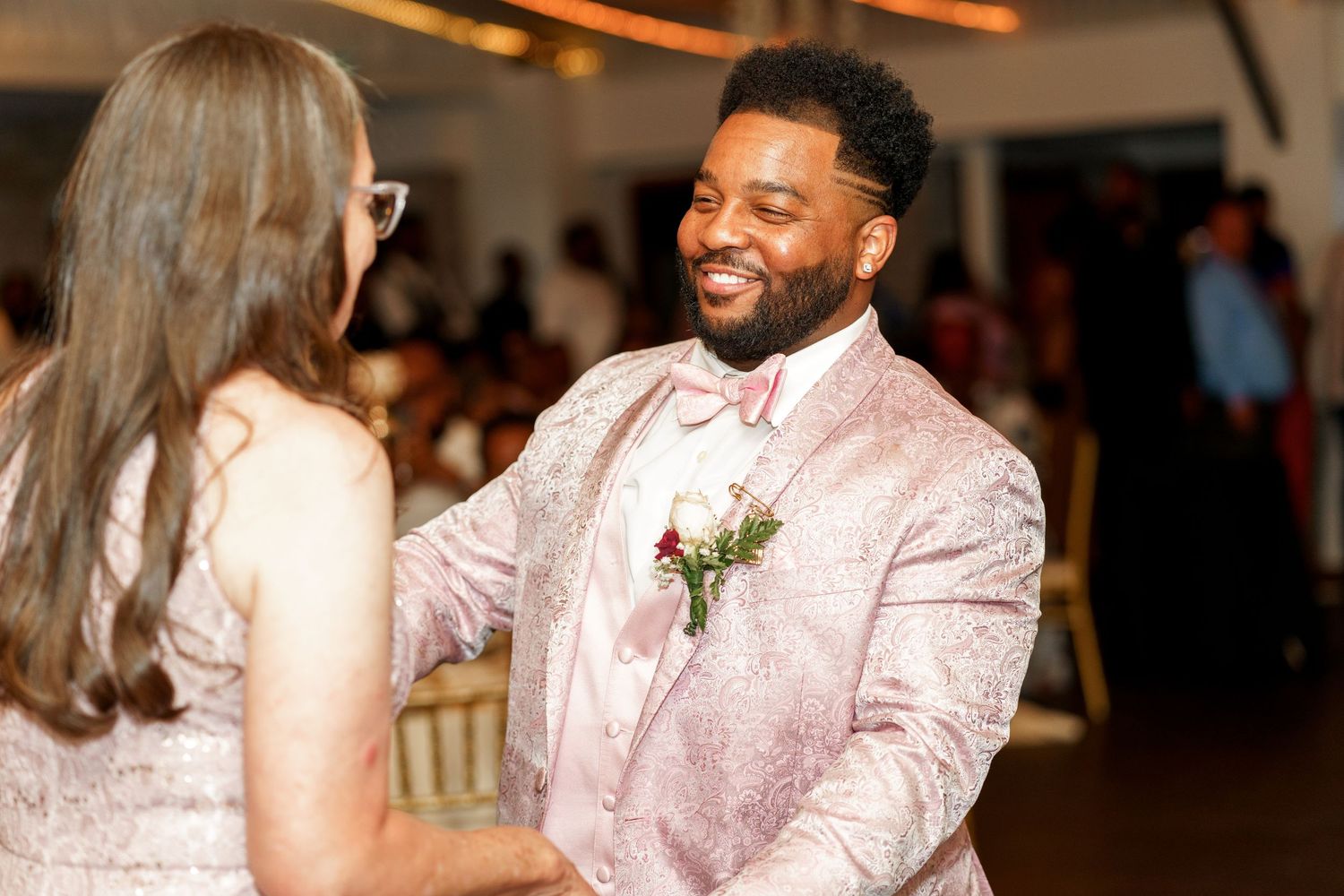 Wedding guest in pink suit dancing with another guest at an elegant reception.