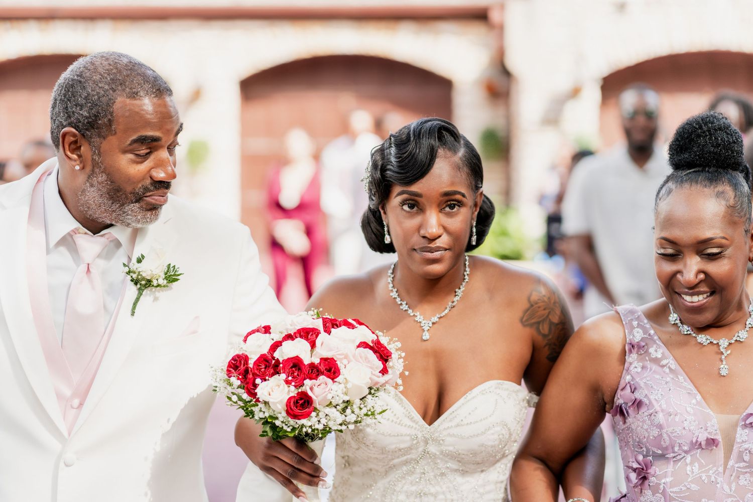 Three wedding participants share a happy moment while walking outdoors near a brick building.