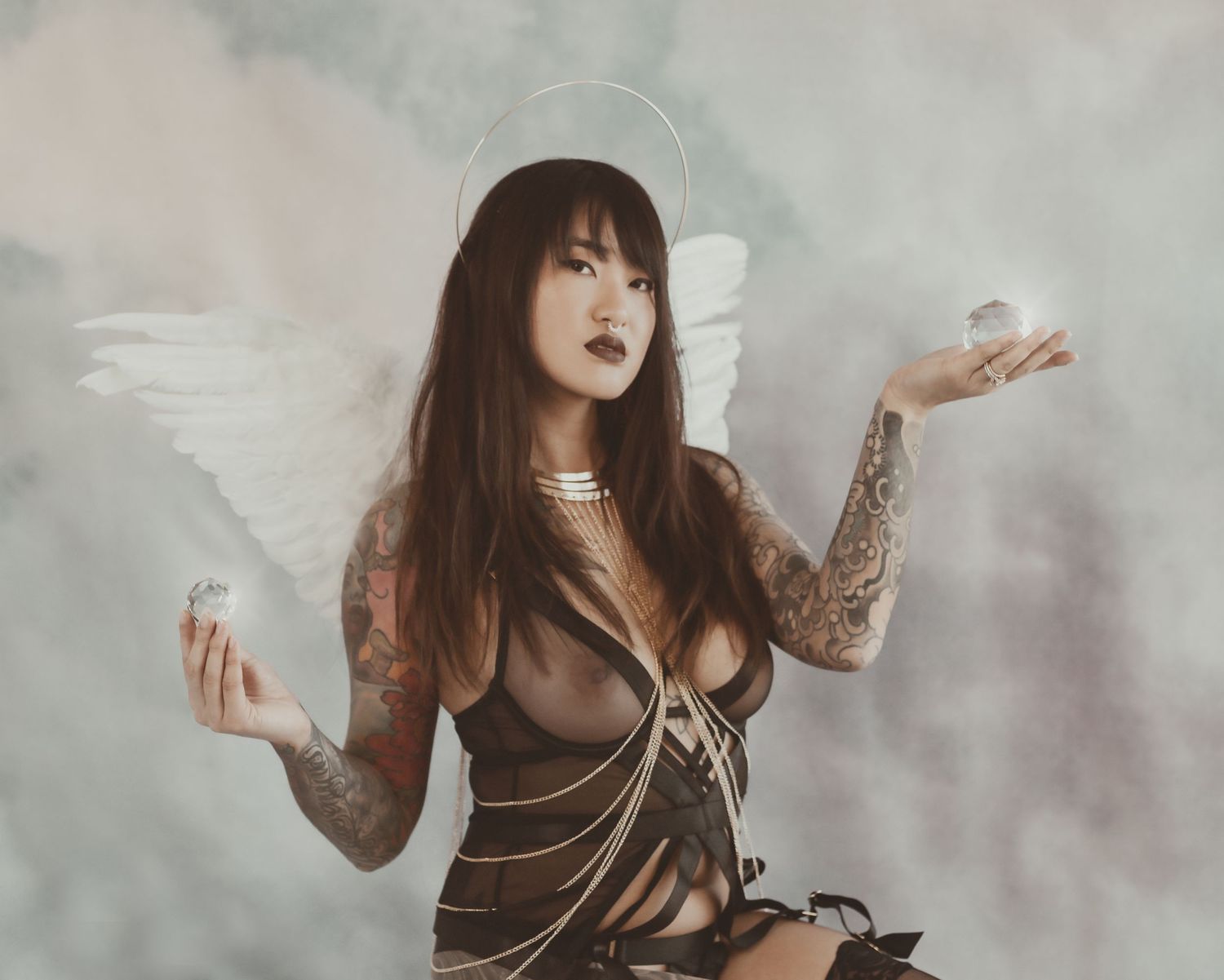 Angelic gothic boudoir pose with dramatic clouds and wing accessories.
