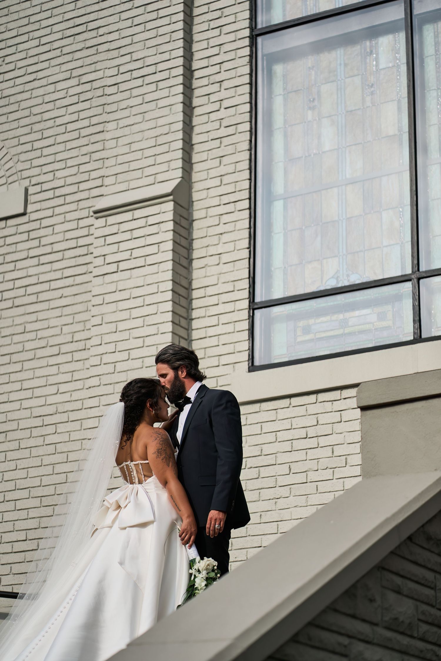 A romantic moment between newlyweds against a white brick wall during their wedding day.