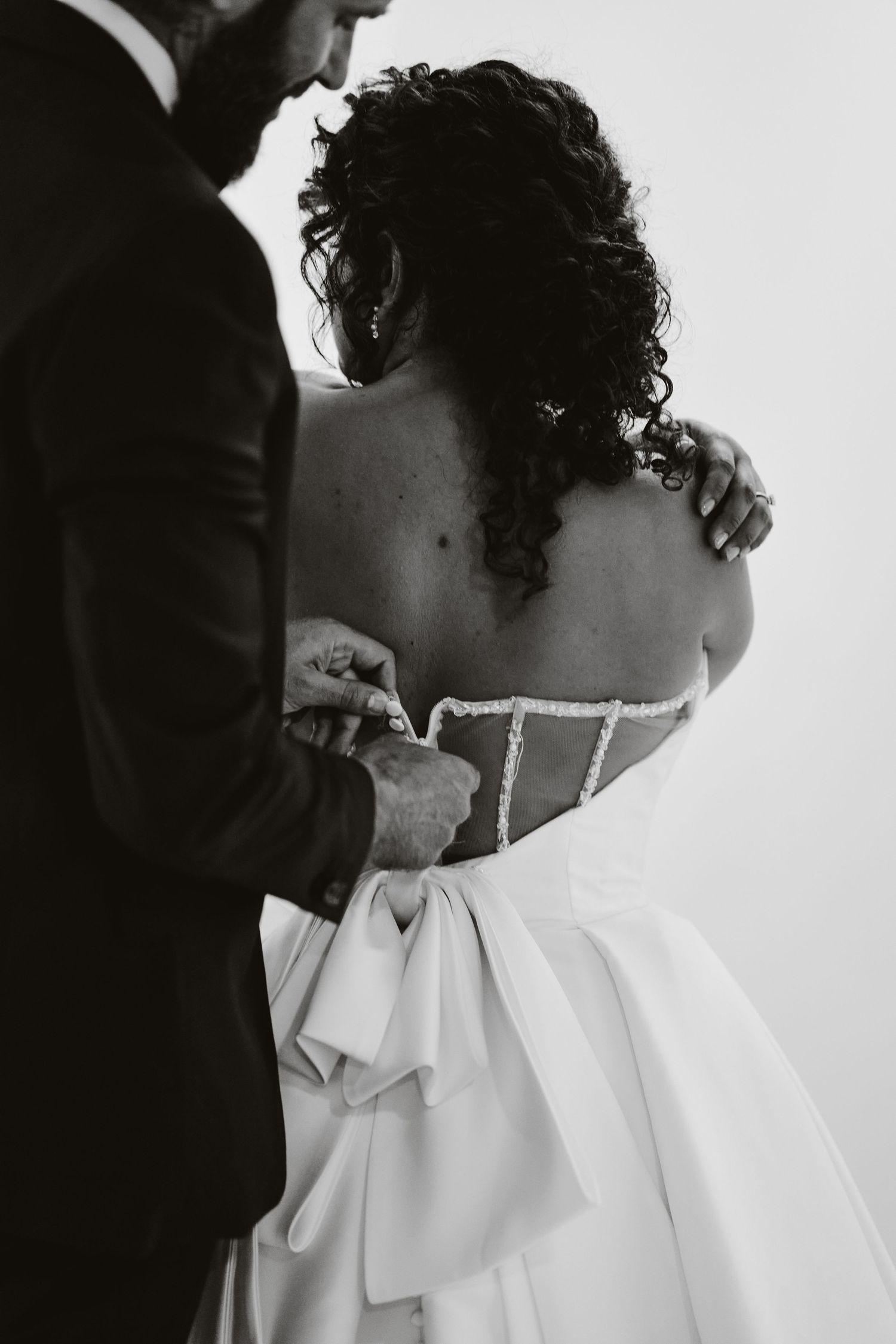 Black and white photographs showing intricate details of a wedding dress being fastened.