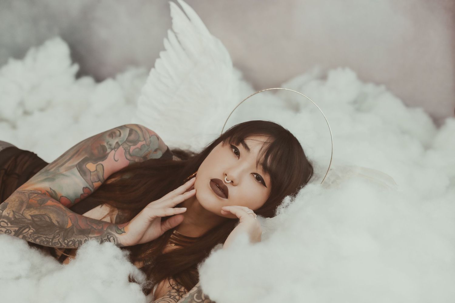 A dramatic close-up portrait showing intricate tattoo work against cloudy white backdrop.