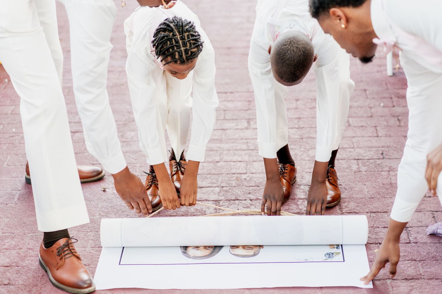 Wedding party members in white suits looking down at photo display on ground.