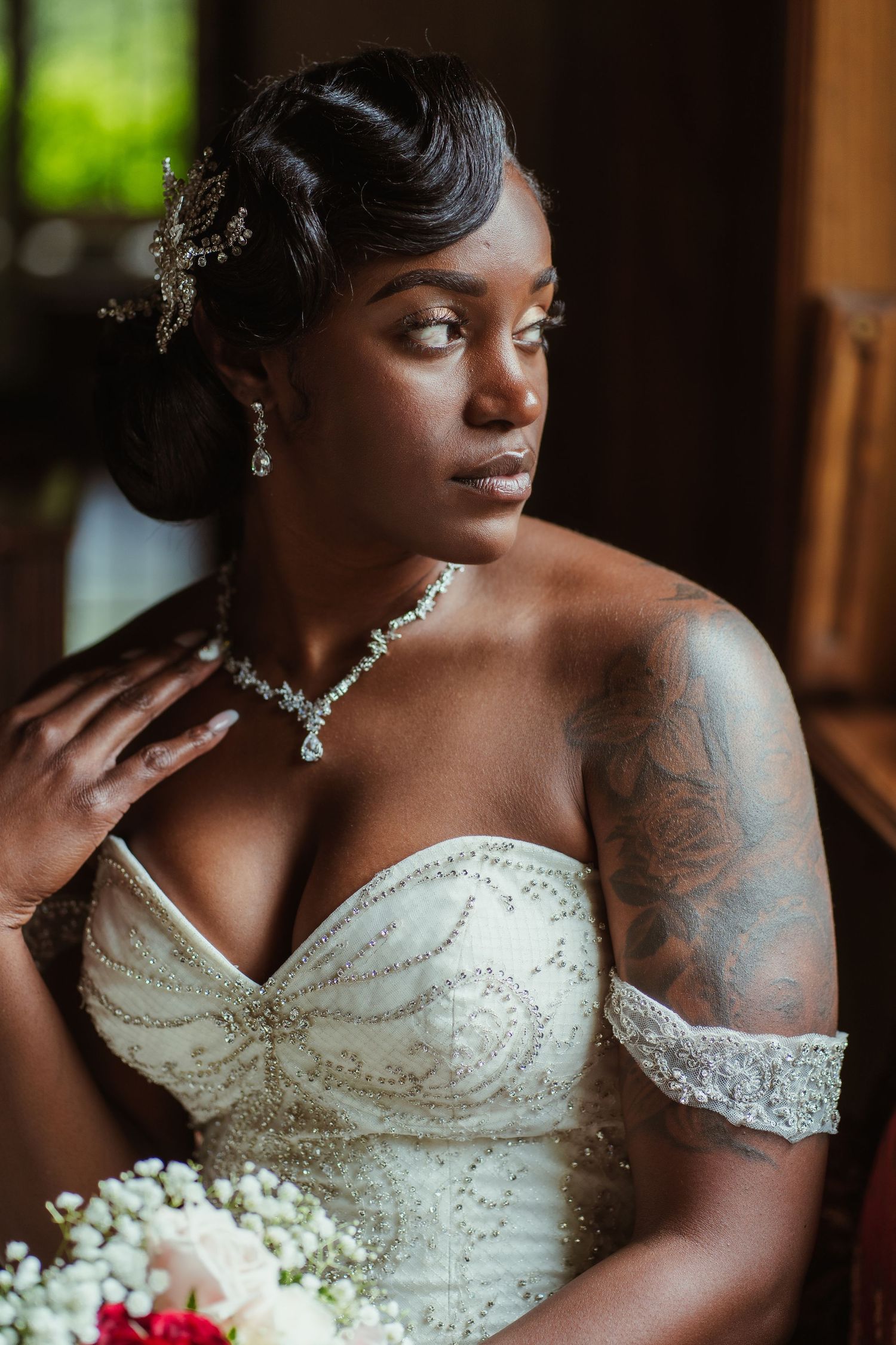 Bride wearing crystal jewelry and strapless gown poses in elegant portrait with natural window light.