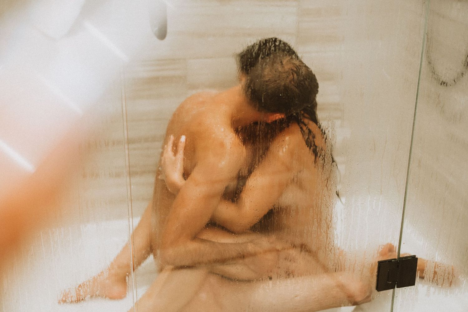 An intimate moment captured in soft focus through a steamy shower glass.
