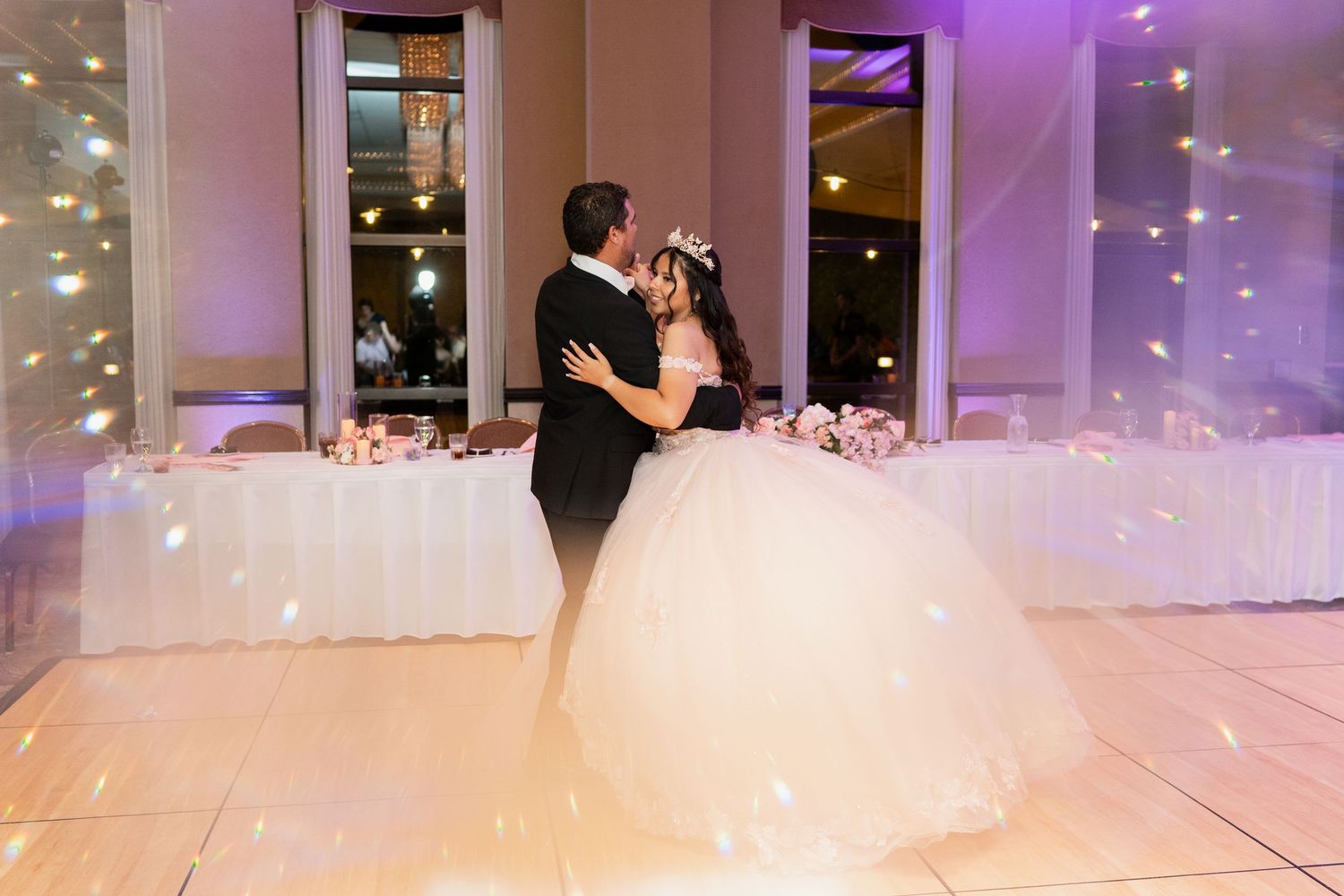 Couples dancing on a white wedding reception dance floor under purple lighting during their celebration.