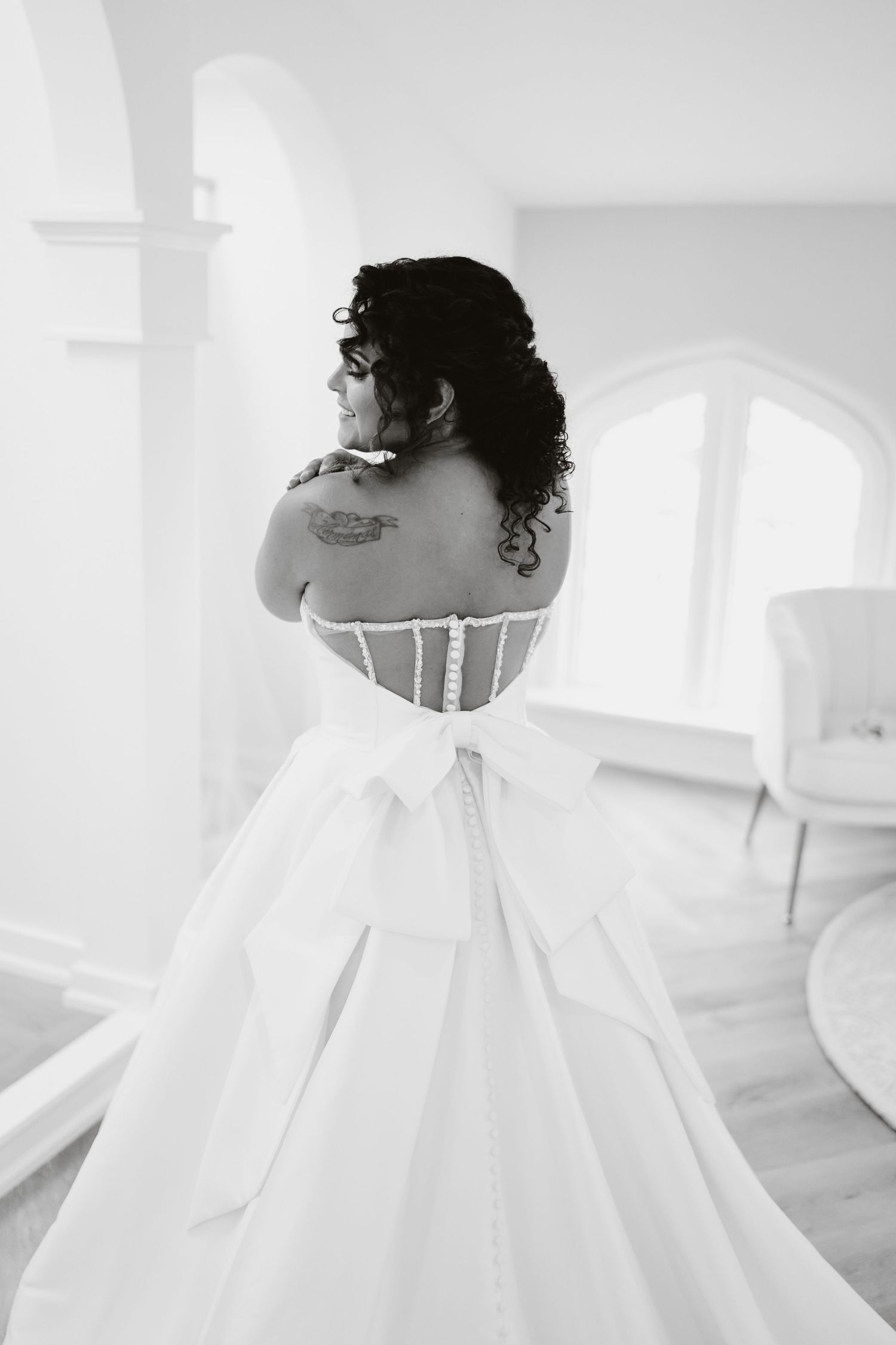 Back view of a bride in a white strapless ballgown with delicate corset detail and visible tattoo.