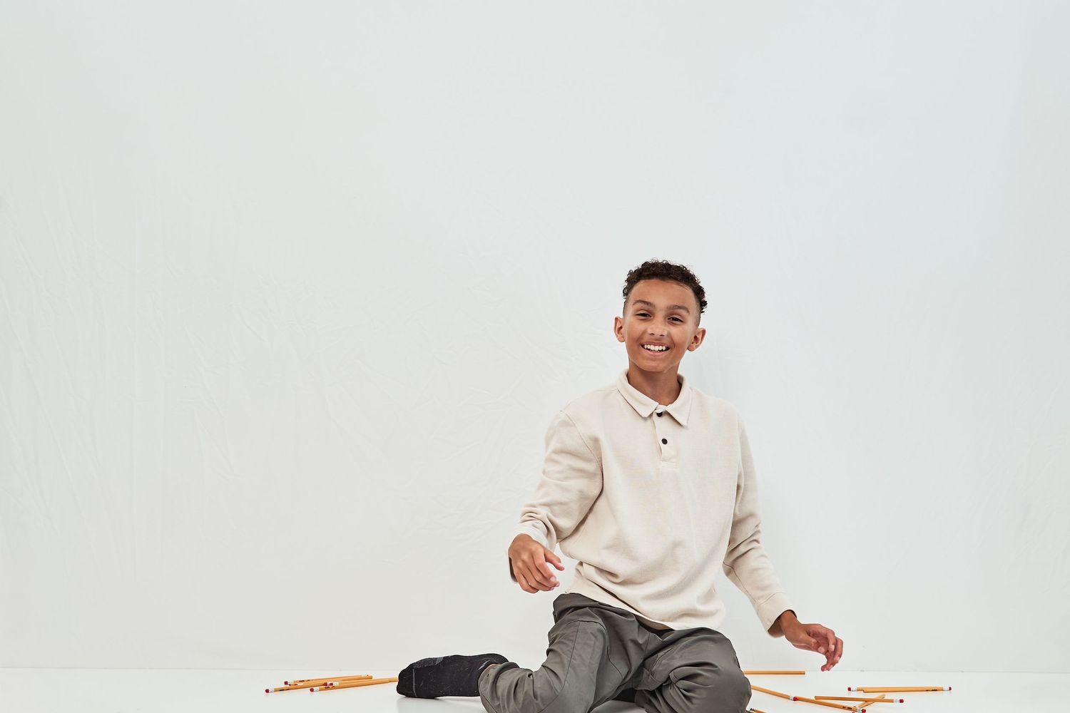 A person sits cross-legged wearing a cream sweater against a plain white background.