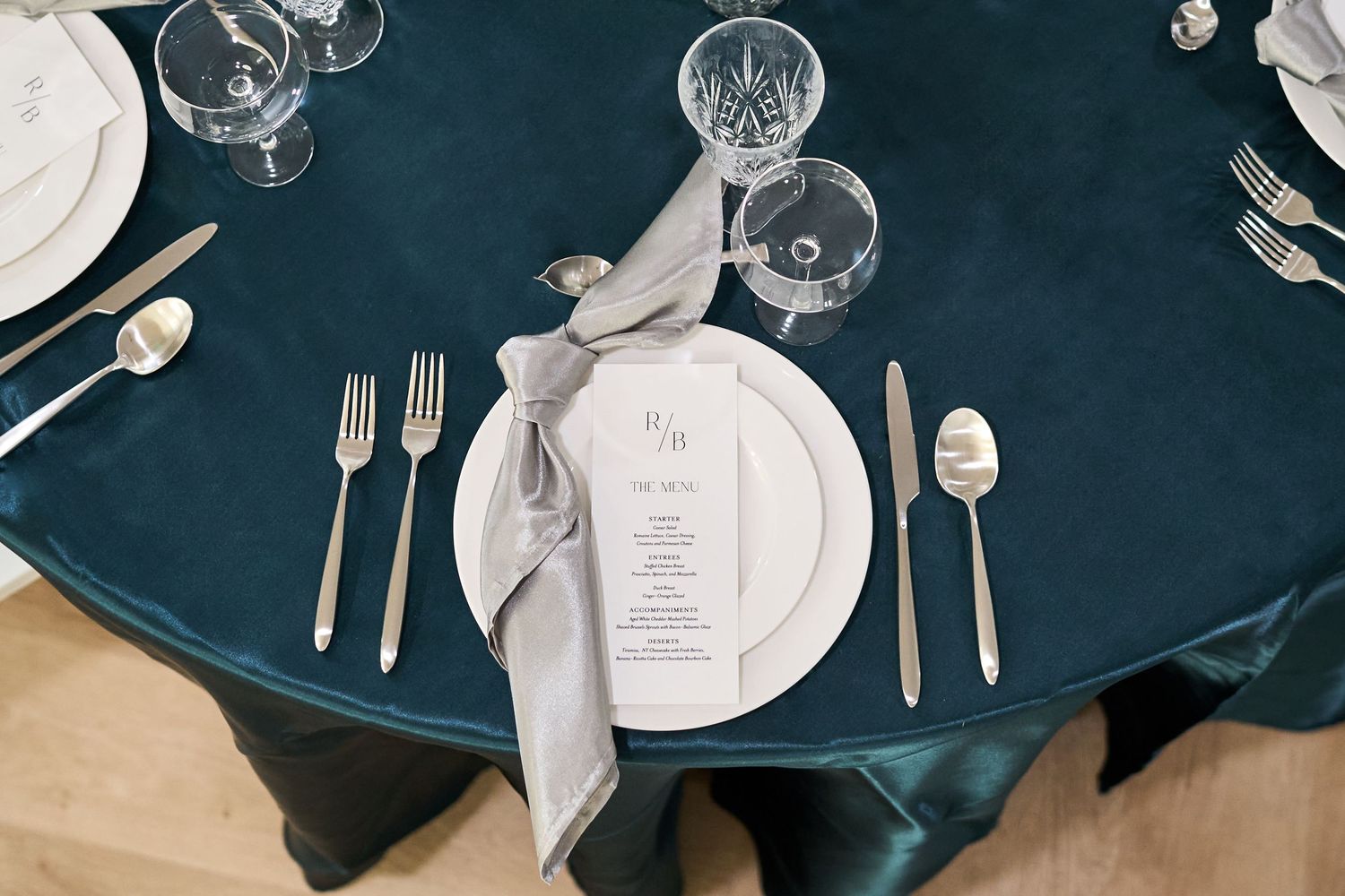 Elegant place settings with navy tablecloth, crystal glasses and silver cutlery at wedding reception.