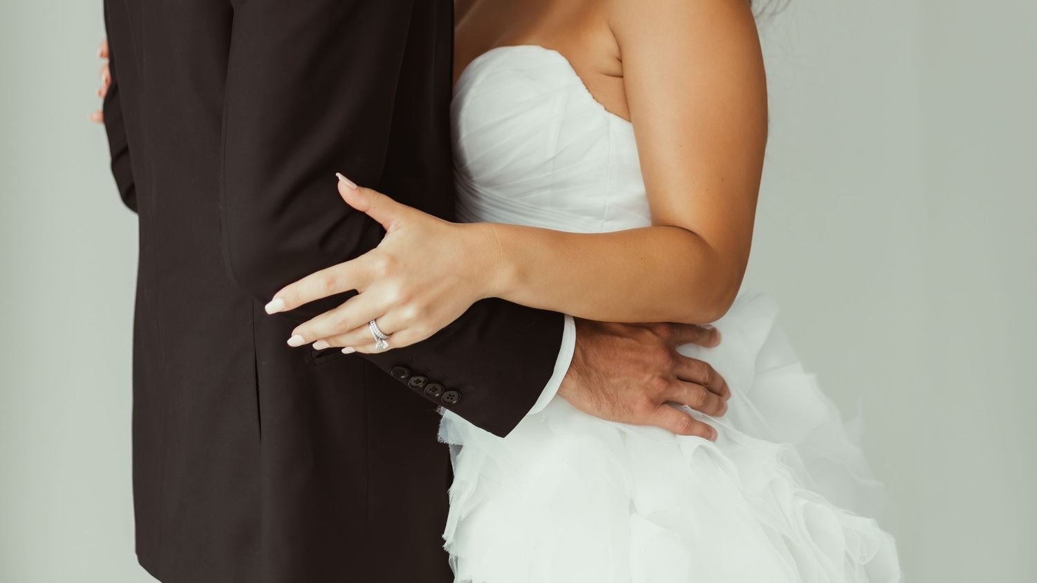 A cropped wedding photo showing the embrace of a couple in formal wedding attire.