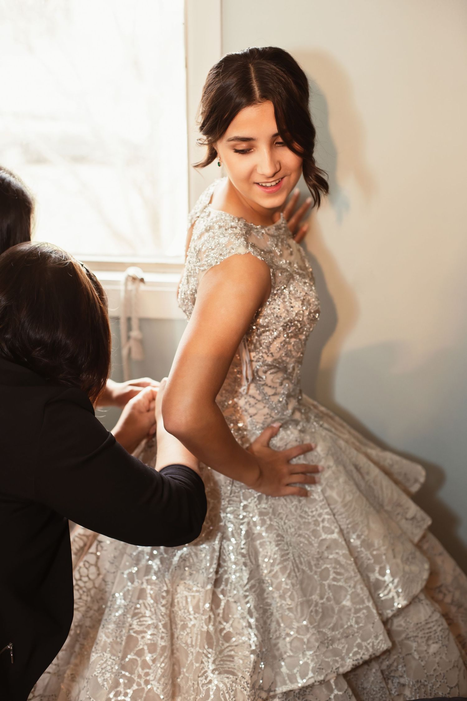 An elegant bridal fitting shows a detailed lace gown being adjusted with care.