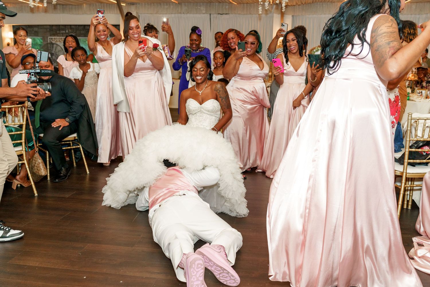 Celebratory dance moves at wedding reception with pink-clad bridal party watching and cheering.