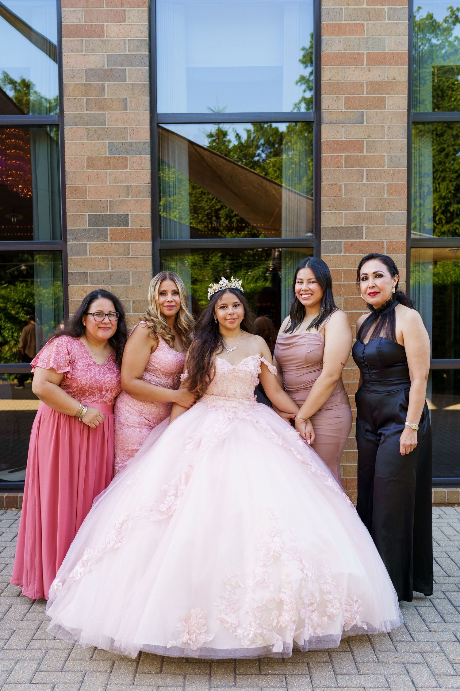 A group in pink bridesmaid dresses and a dramatic pink ball gown pose together outside a brick building.