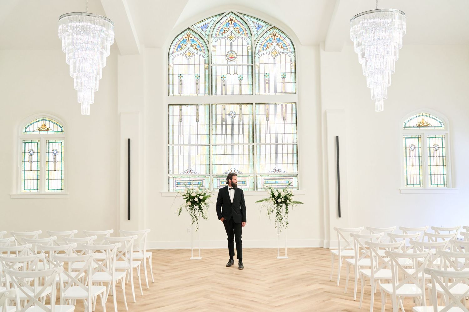 Elegant chapel interior with stained glass windows, crystal chandeliers, and white chairs set for ceremony.