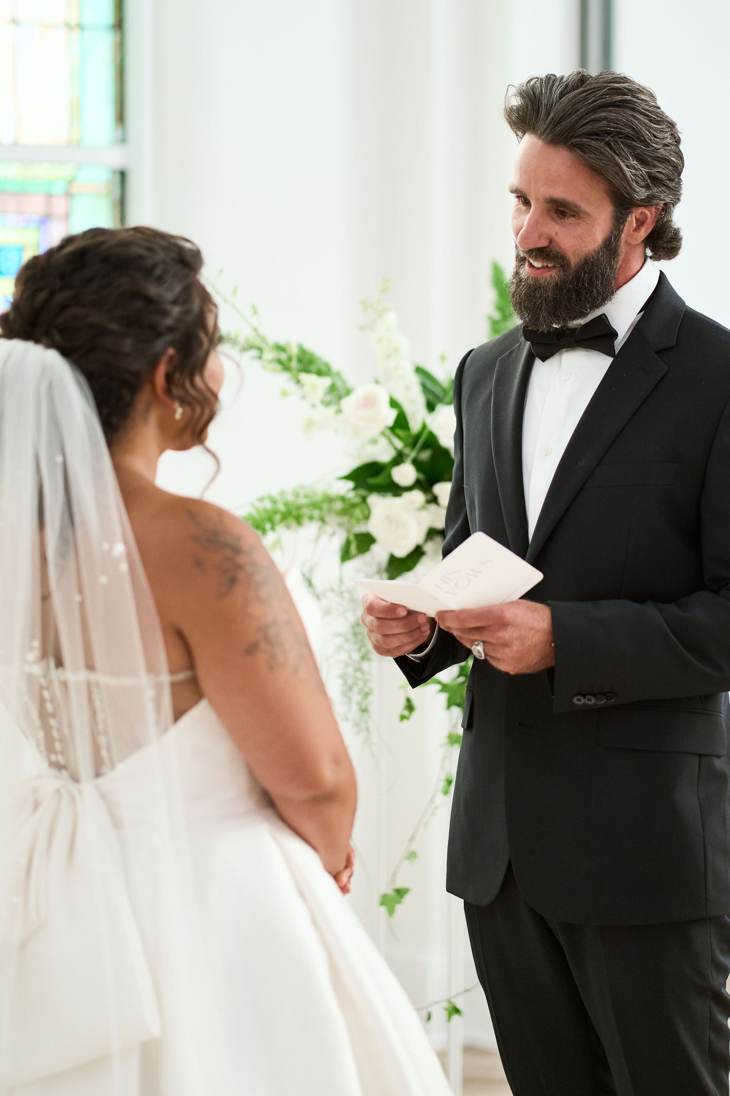 Bride in white dress and groom share emotional first look reactions in bright indoor setting.