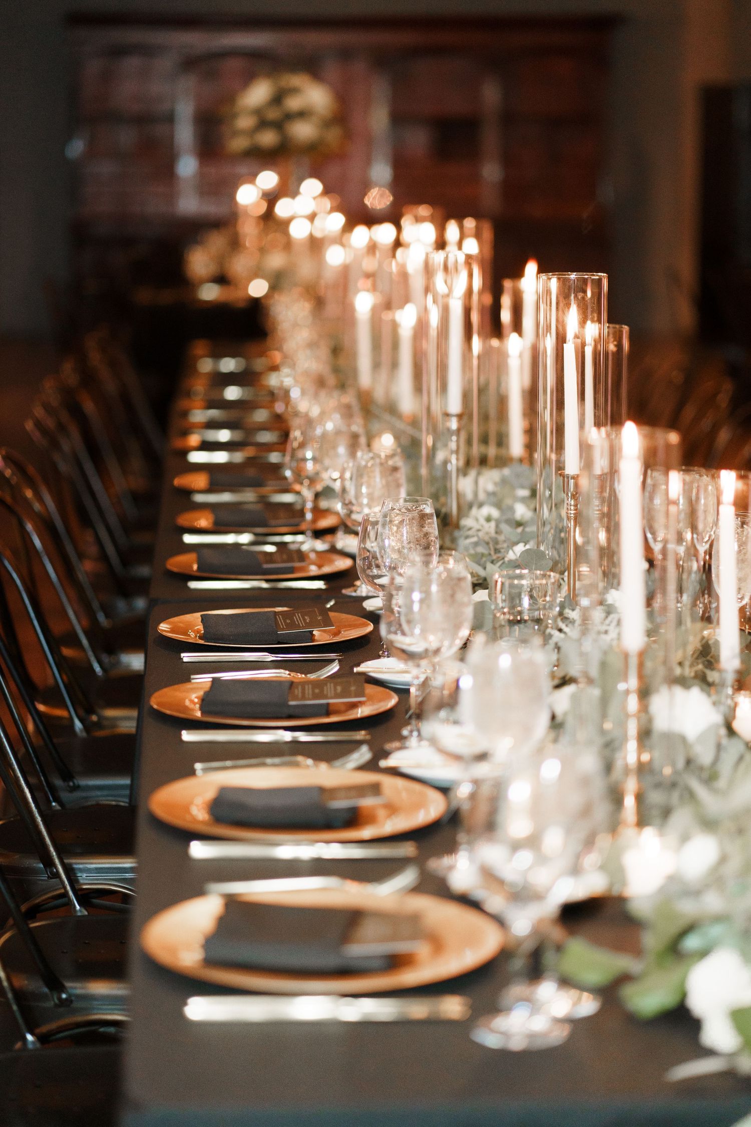 Elegant table setting with black chargers, white plates, and glowing candlesticks creating a romantic dining atmosphere.