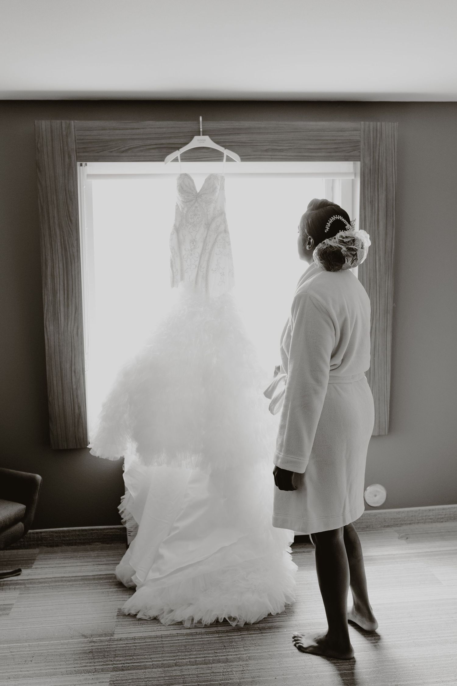 A wedding dress hangs illuminated in a doorway as someone stands before it in a robe.