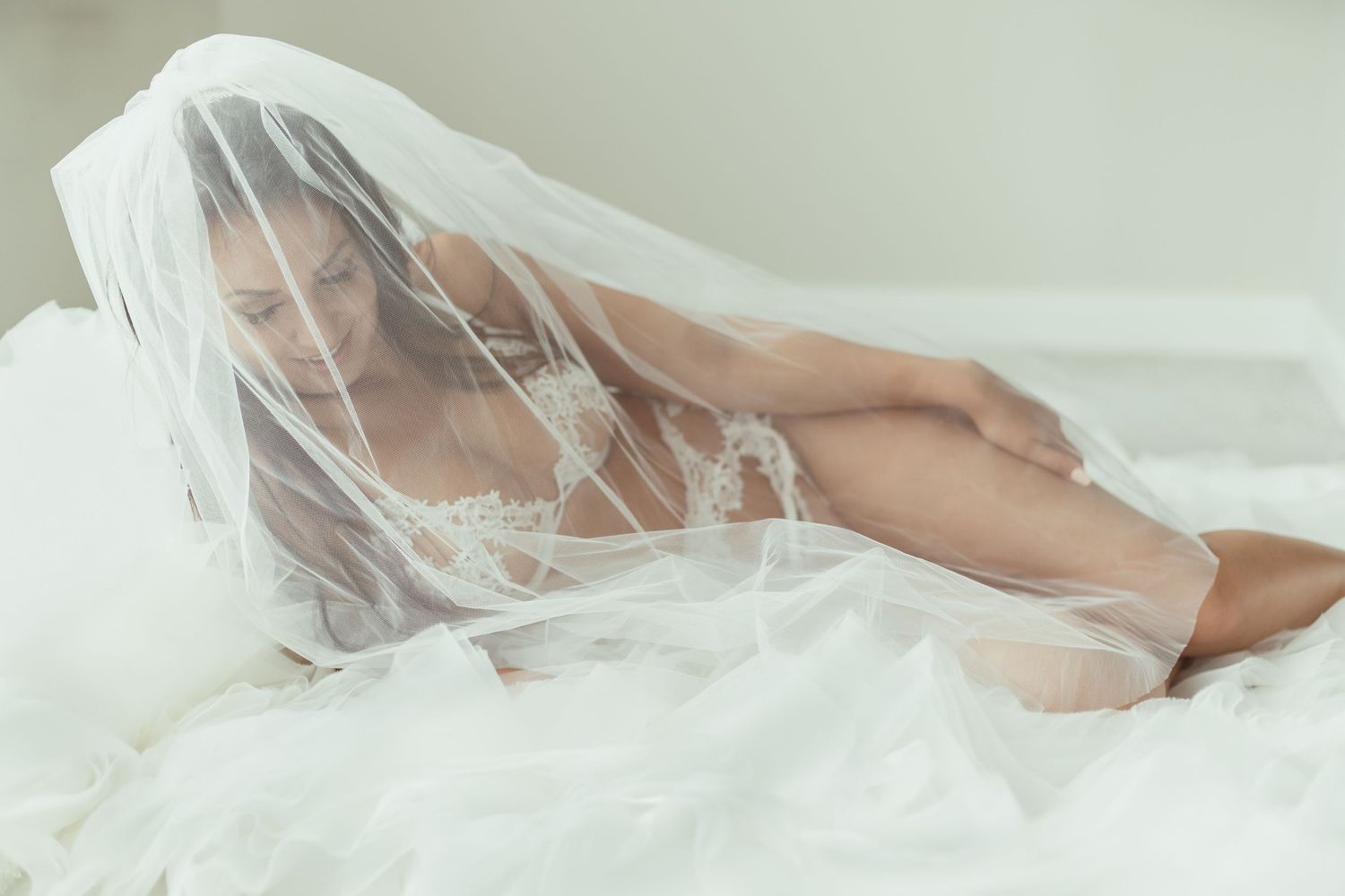 Artistic boudoir photograph with flowing white veil and soft lighting effects.