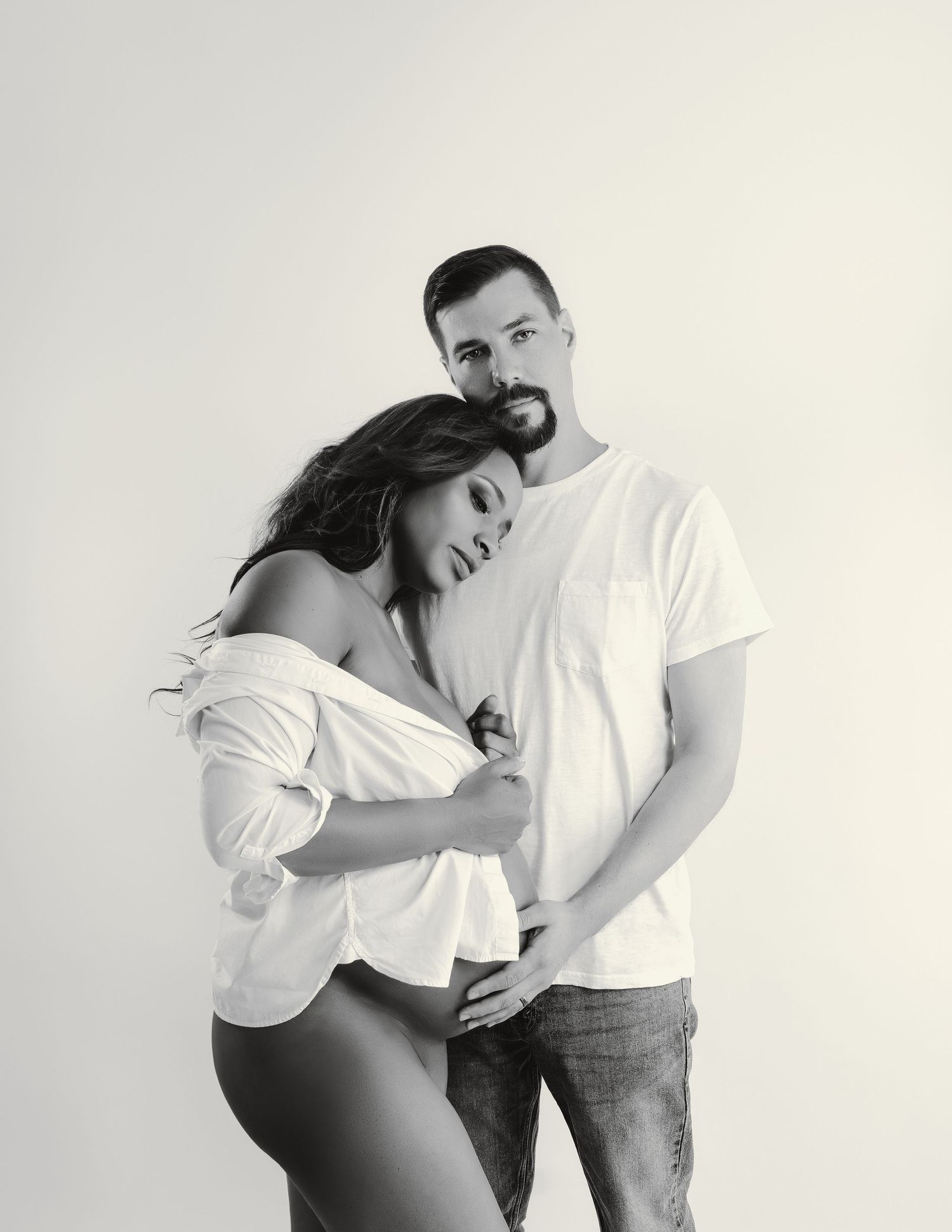 Tender black and white portrait of a couple embracing against a light background.