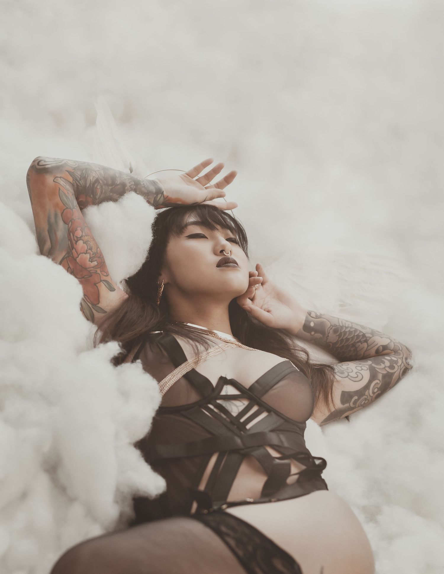 Dramatic fashion portrait with model in dark lingerie posed against cloudy backdrop.