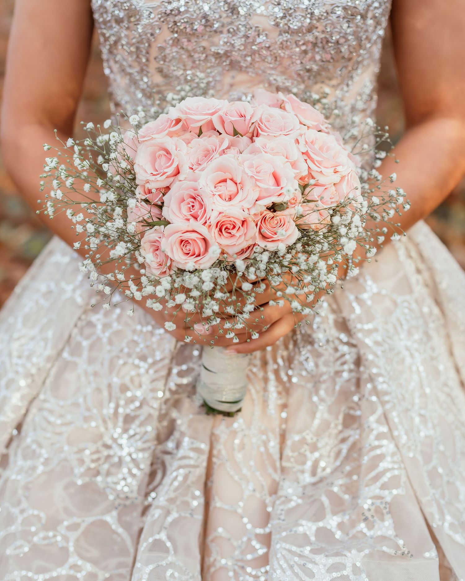 Close-up of pink rose and baby's breath wedding bouquet against a beaded wedding dress.