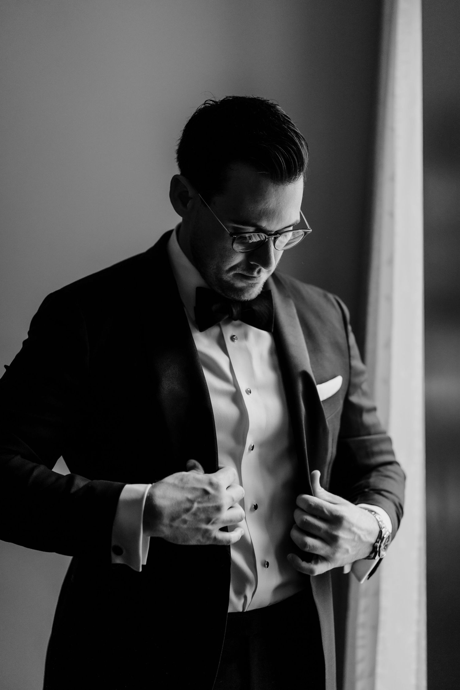 Black and white sequence of a person in a suit adjusting their tie and checking their phone in dramatic lighting.