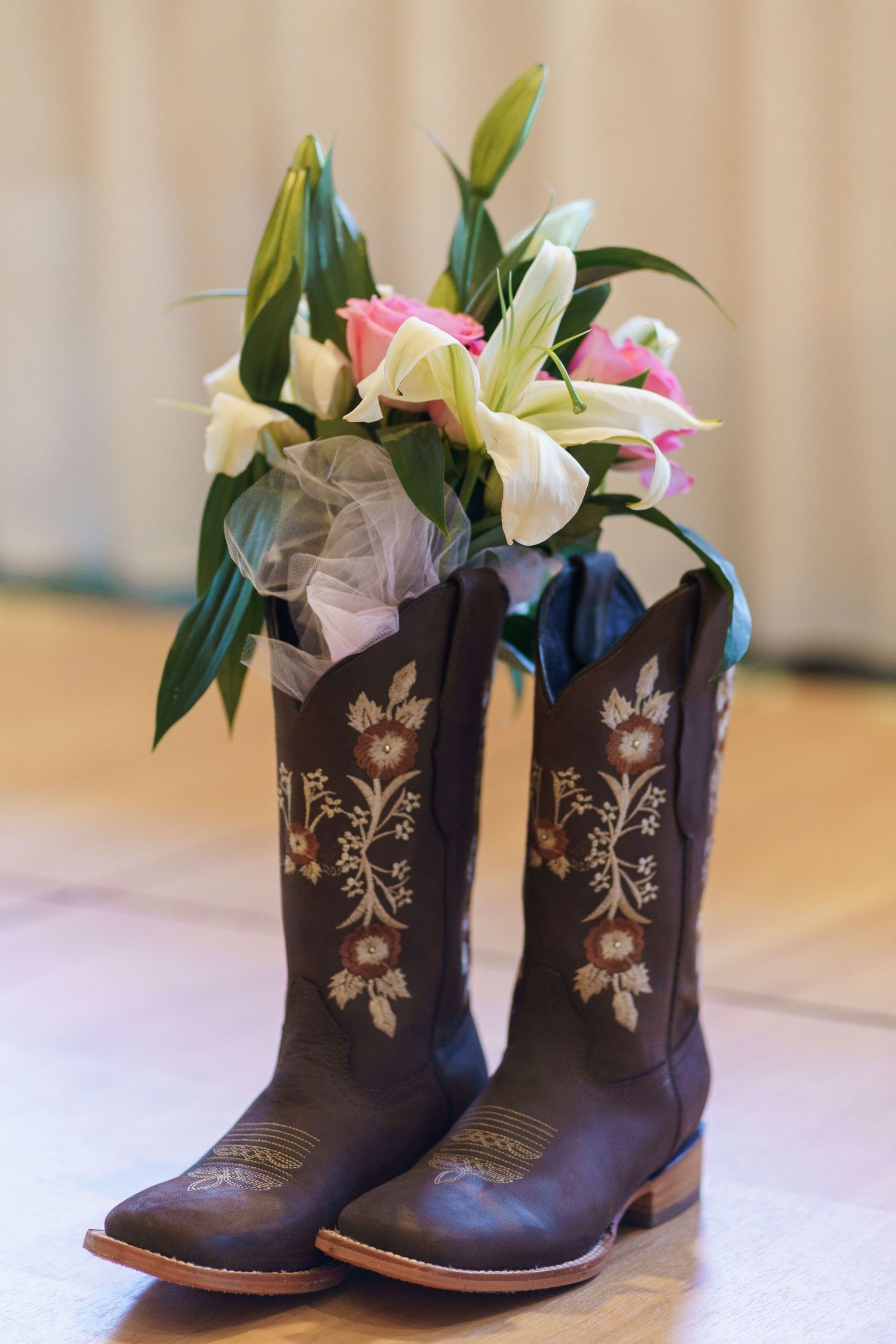 Brown cowboy boots with floral embroidery filled with fresh lilies and pink flowers.
