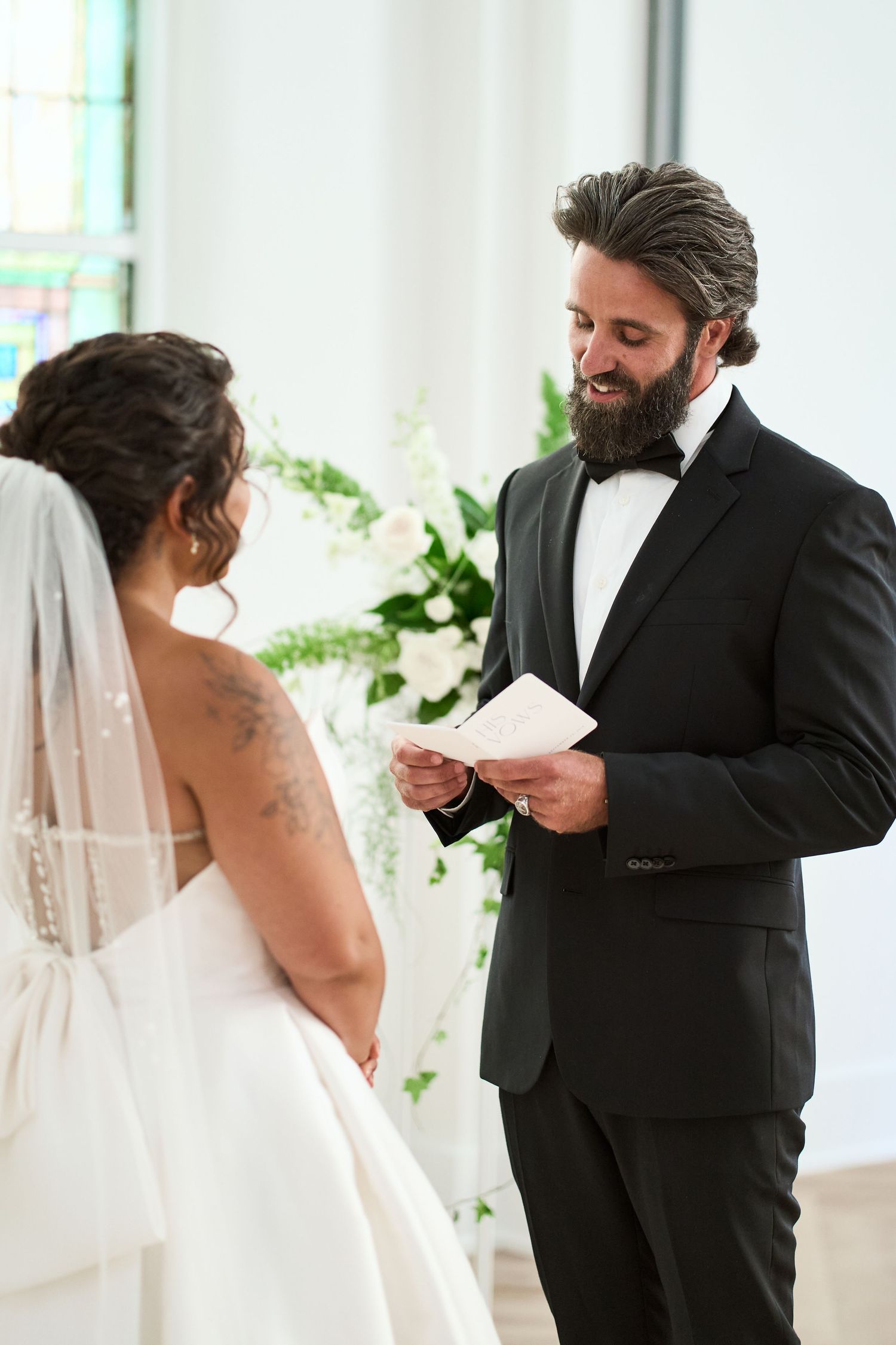 Wedding ceremony moment at a light-filled chapel with soft white decor and floral arrangements.