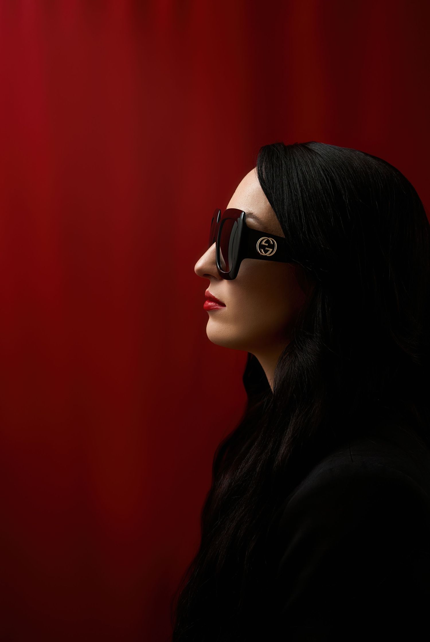 Side profile portrait with sunglasses against dramatic red background in dark moody lighting.