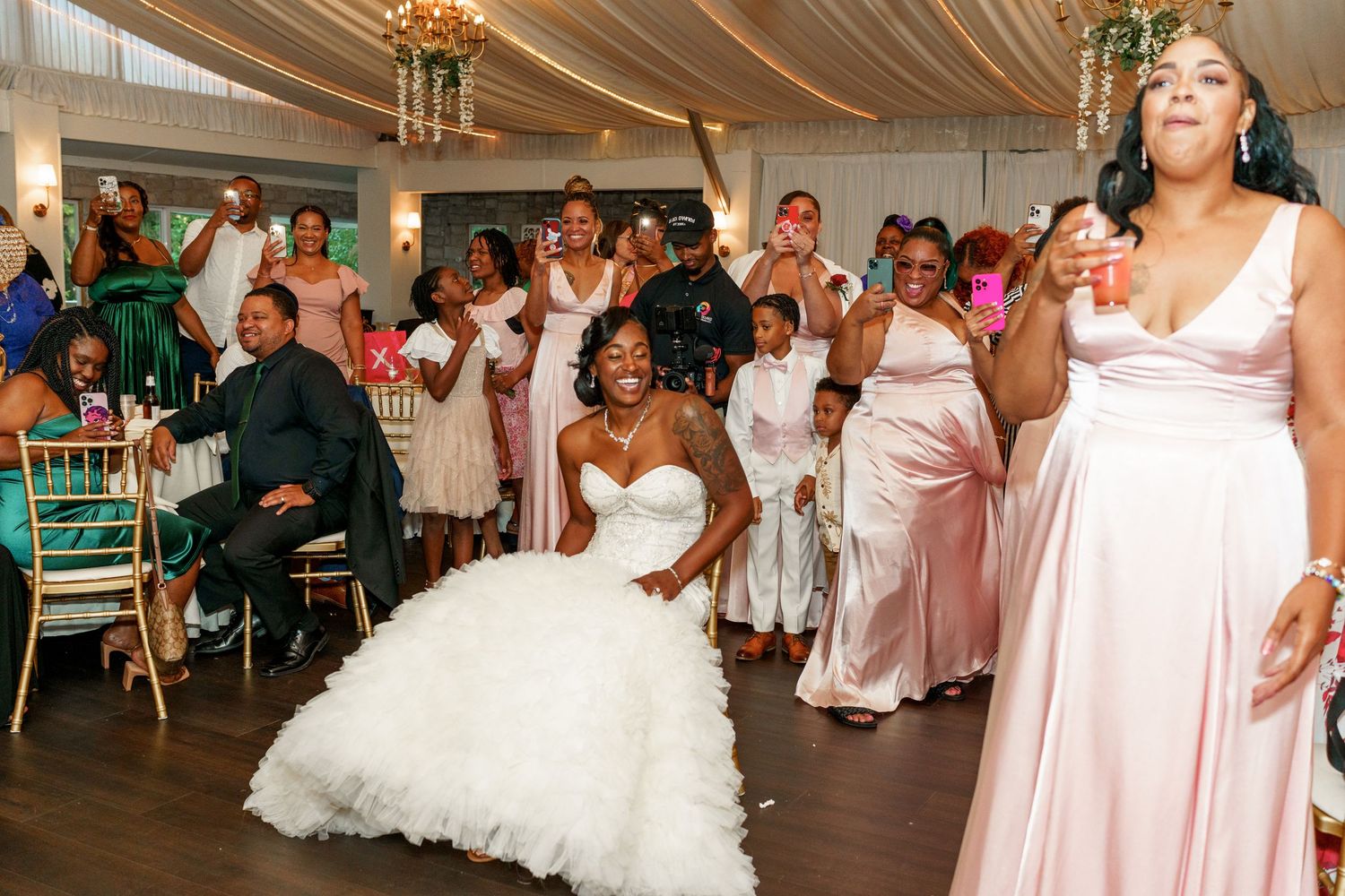 Wedding party celebrates with enthusiastic dancing in an elegant reception venue with pink decor.