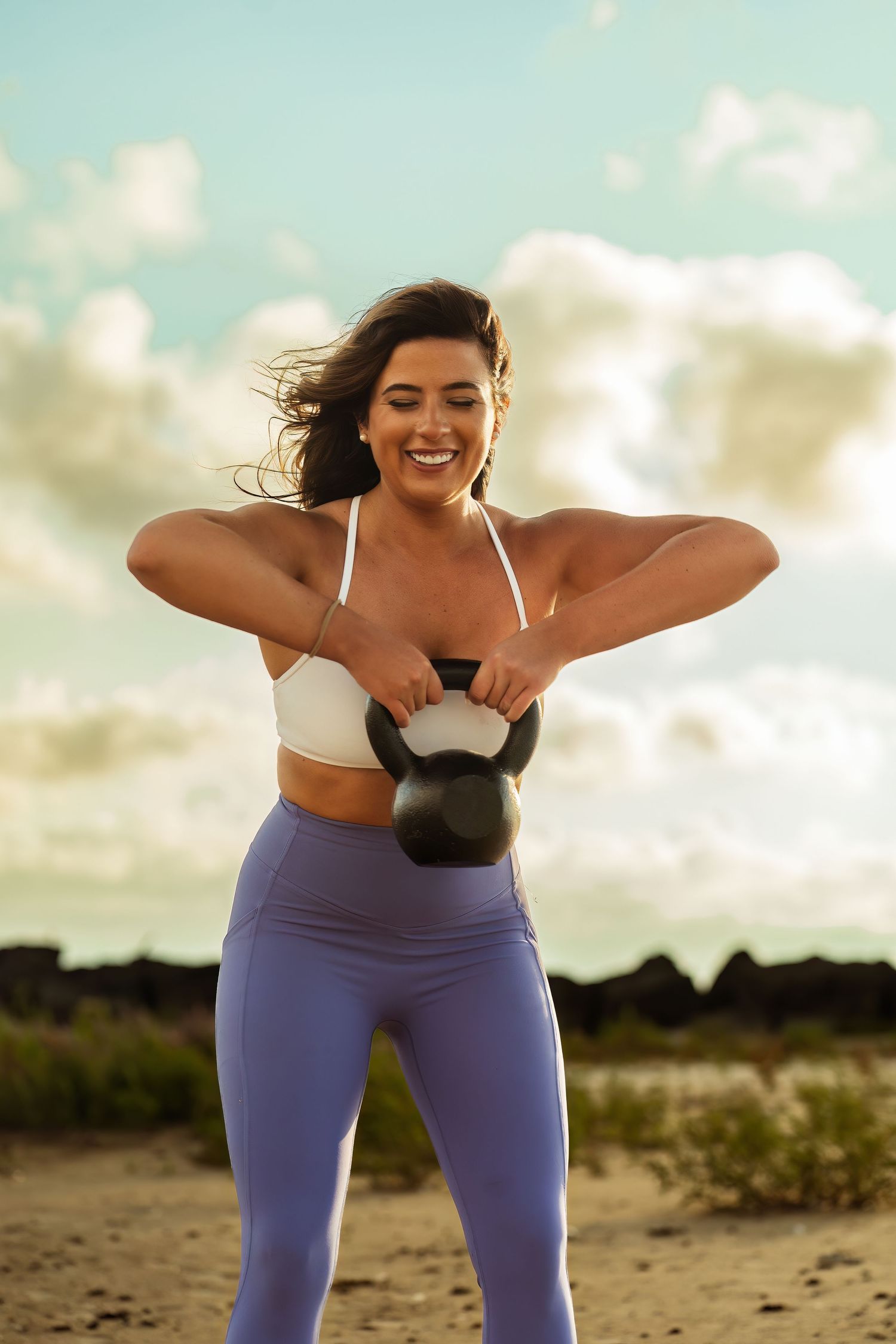 Energetic fitness enthusiast exercises with kettlebell against cloudy beach backdrop.