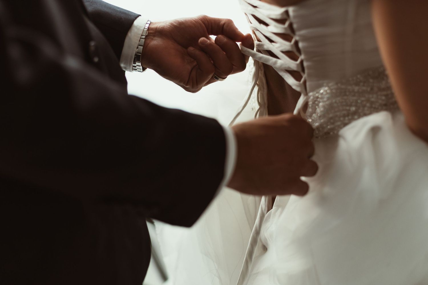 Detail shot of hands tying white satin wedding dress laces.