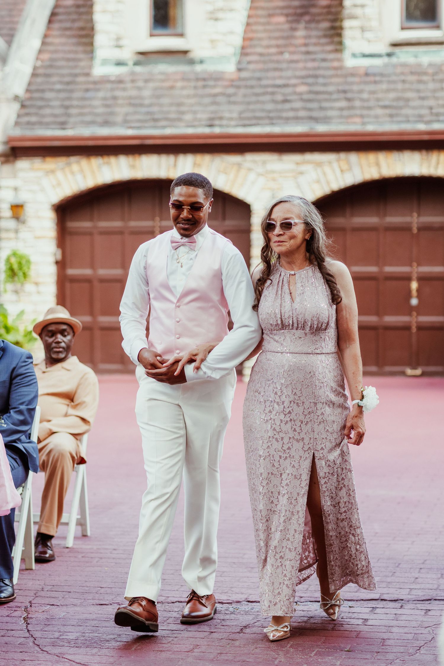 Elegantly dressed couple walks together on red brick pathway at formal event.