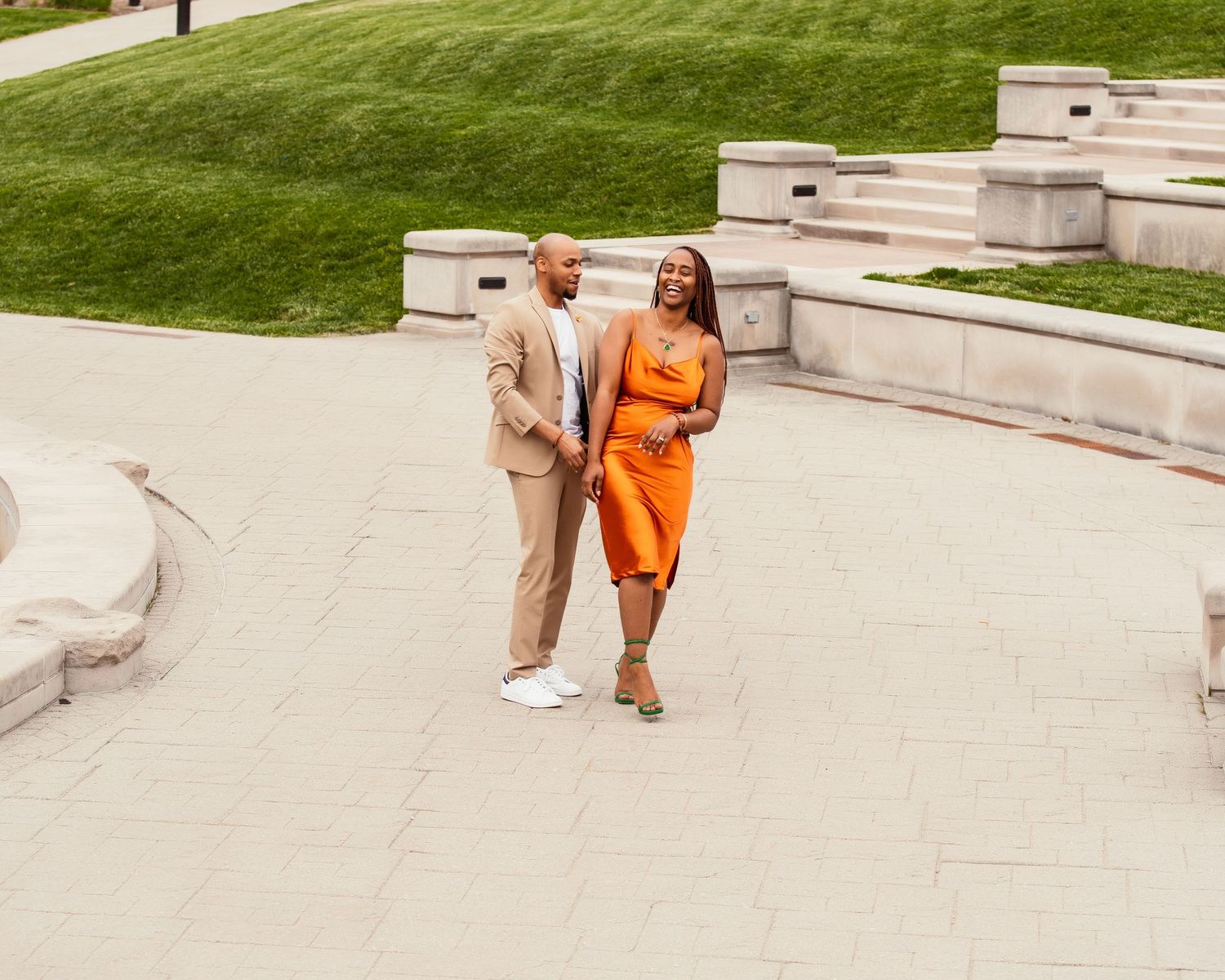 Couple walking together on stone steps wearing coordinated orange dress and beige suit.