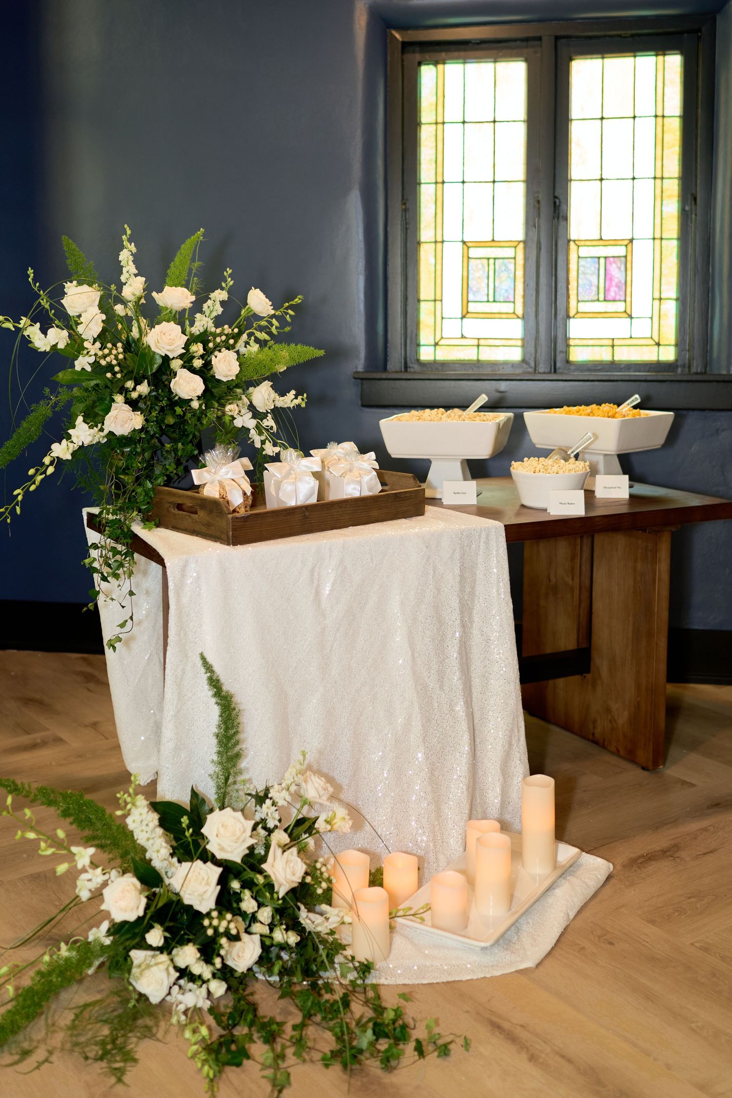 Elegant wedding reception table with white floral arrangements, candles, and stained glass windows in background.