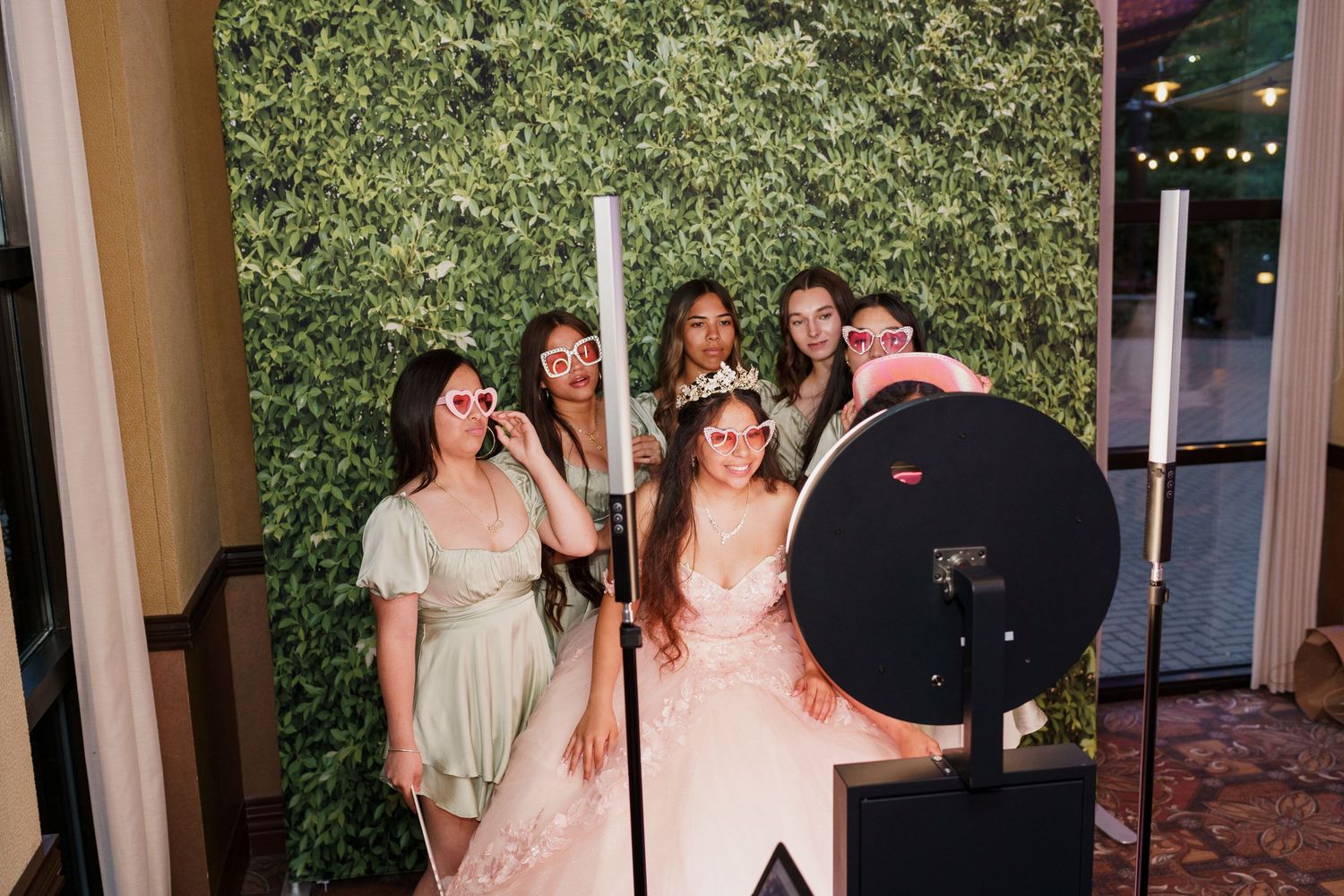 Group of people posing with selfie ring light against greenery backdrop at formal event.