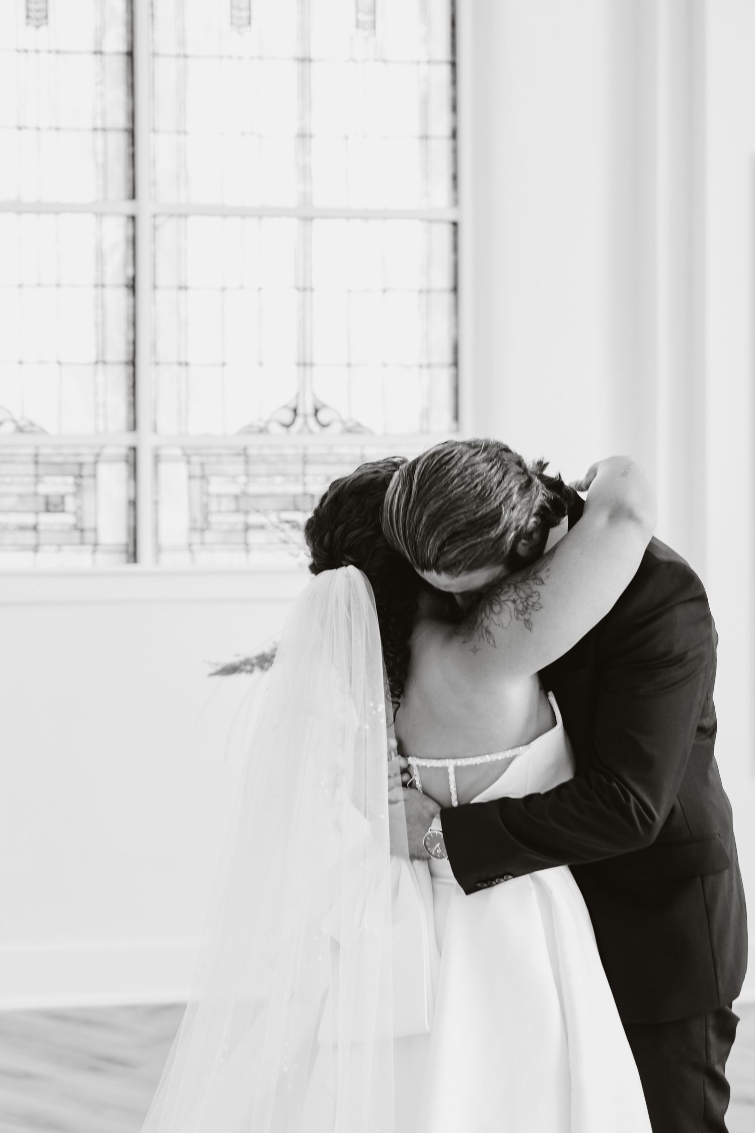 Black and white romantic wedding moment captured near a large window.
