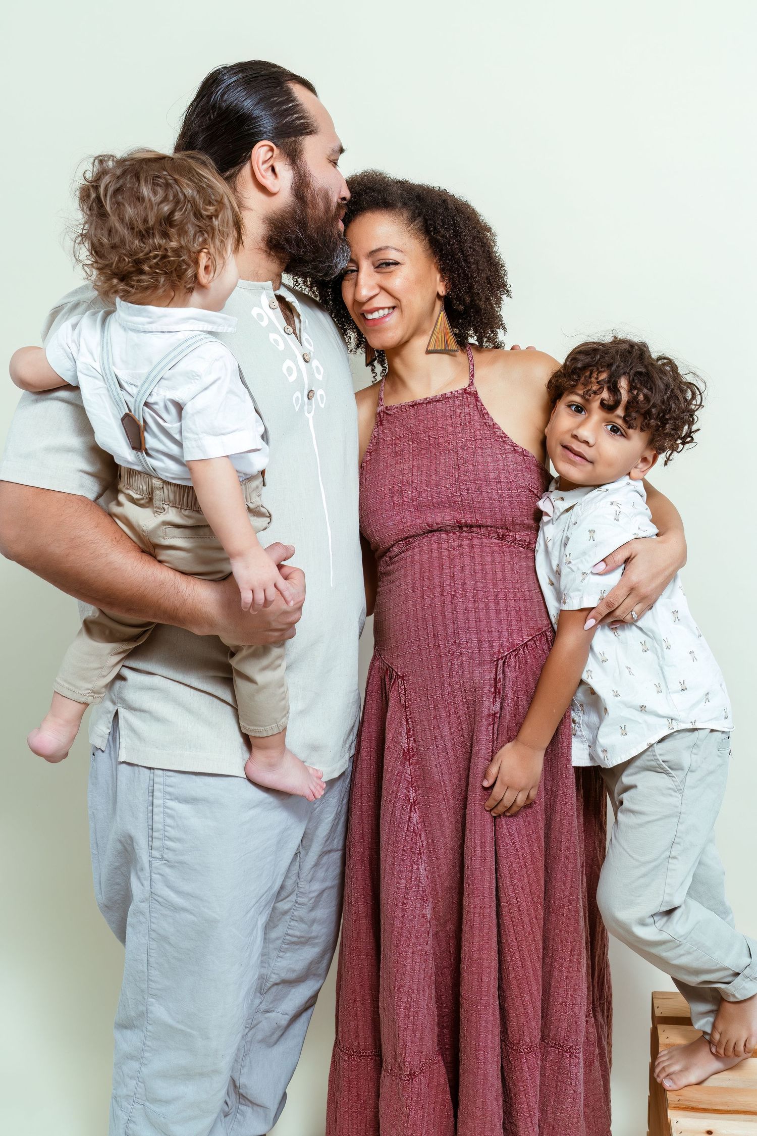 A family shares tender moments together in a series of candid poses against a white wall.