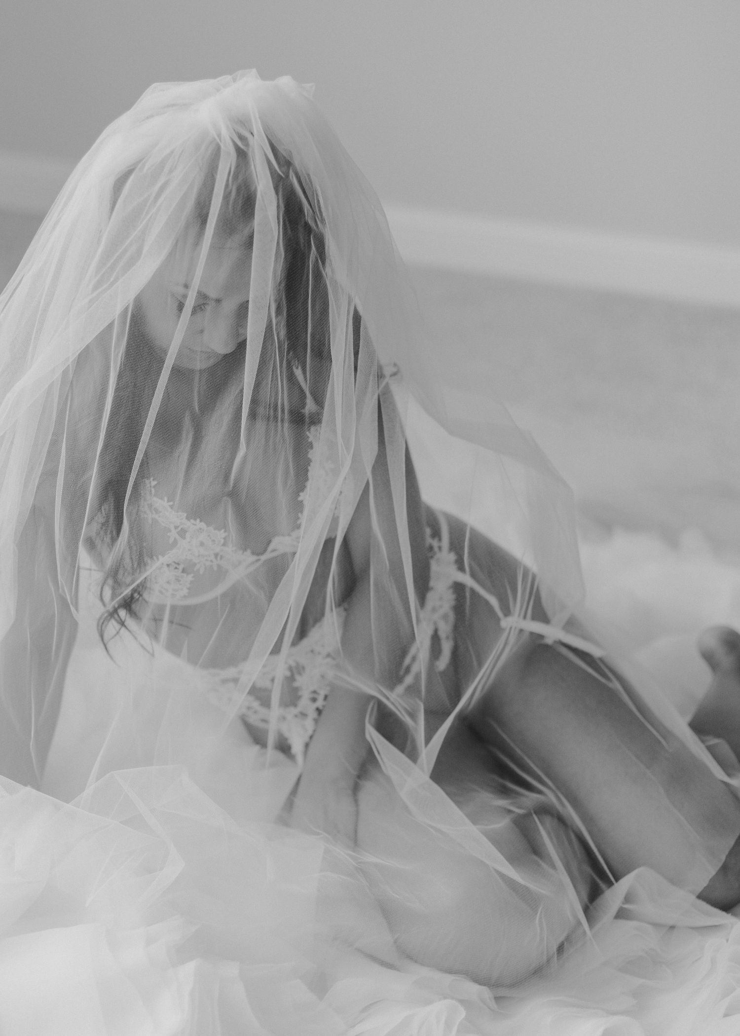 Artistic black and white bridal boudoir photo with delicate veil creating ethereal mood.