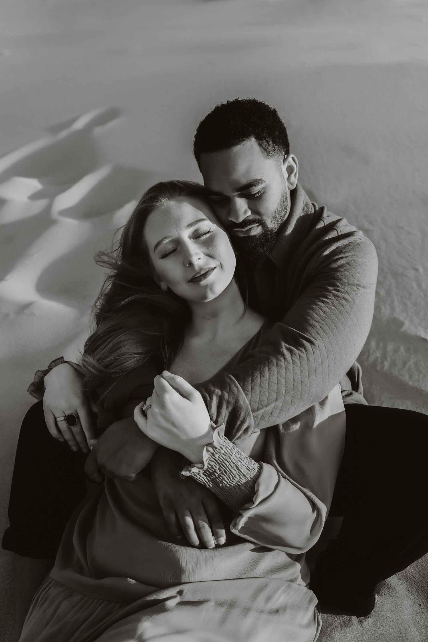 Intimate black and white portrait of a couple embracing on a sandy beach.