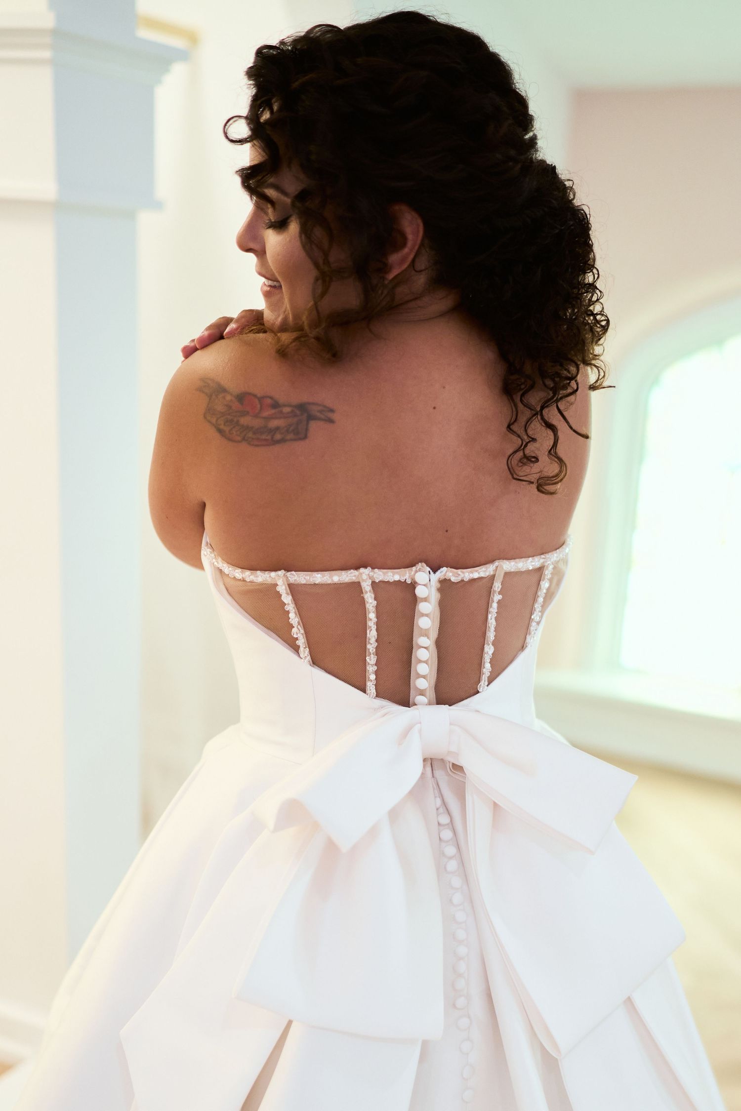 Back view of a bride's sheer corset wedding dress showing intricate button details and a large bow.