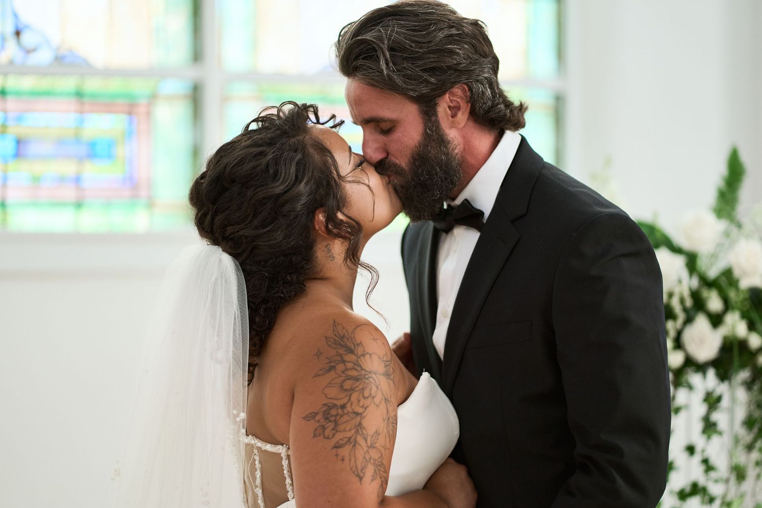 An intimate wedding moment captured in a chapel with stained glass windows in the background.