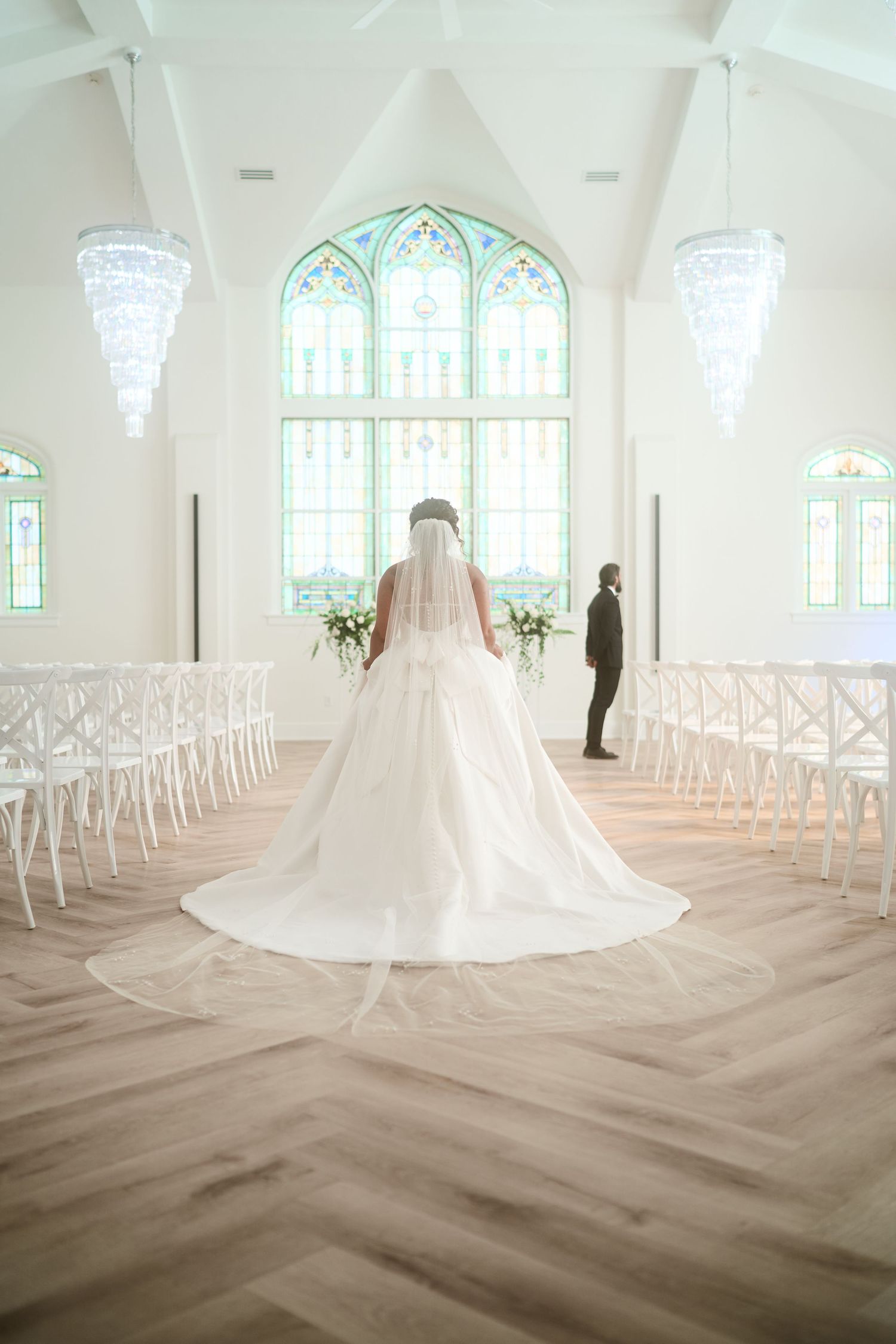 An elegant chapel interior with crystal chandeliers and a long center aisle lined with white chairs.
