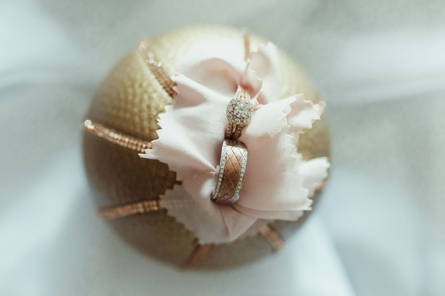 Wedding ring displayed on a champagne-colored decorative sphere with white ribbon accent.