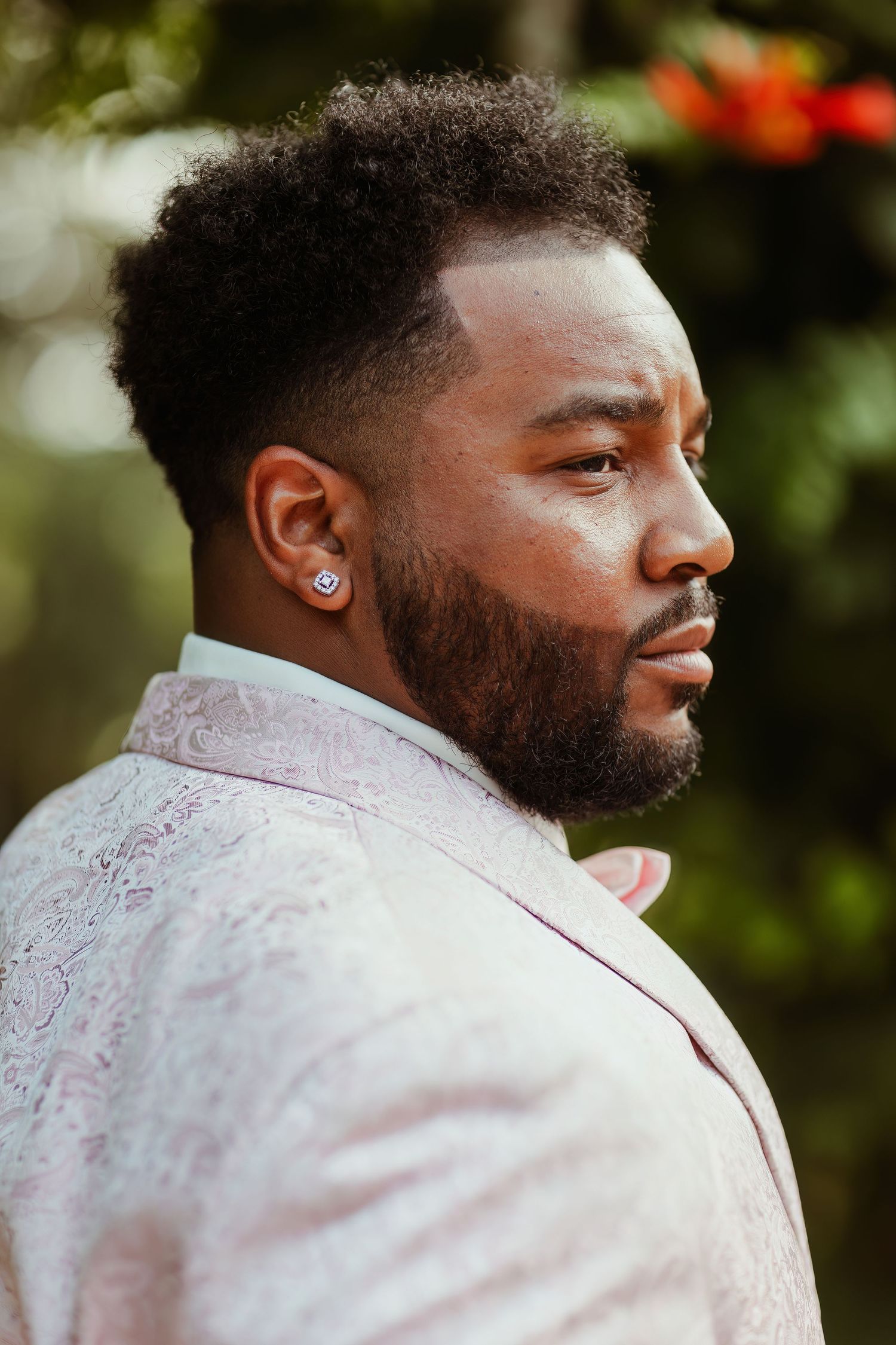 Profile portrait of person wearing light pink jacquard suit jacket in garden setting.
