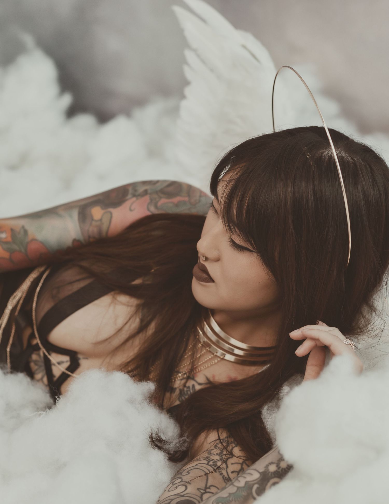 A artistic portrait featuring a model with tattoos surrounded by white clouds and wearing a halo.