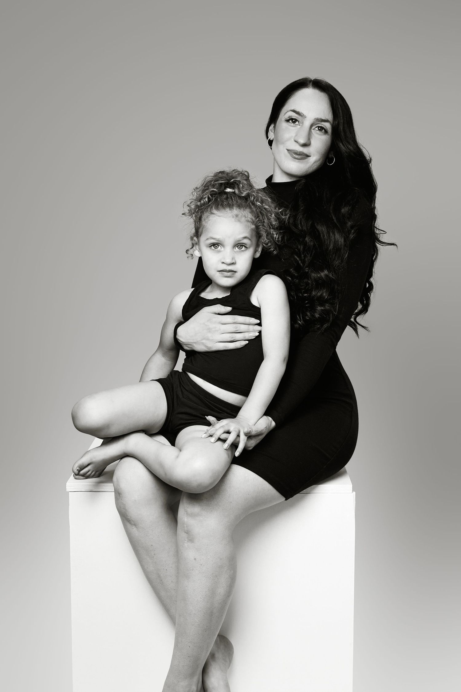 Black and white artistic portrait series showing intimate mother and child poses against minimalist studio backdrop.