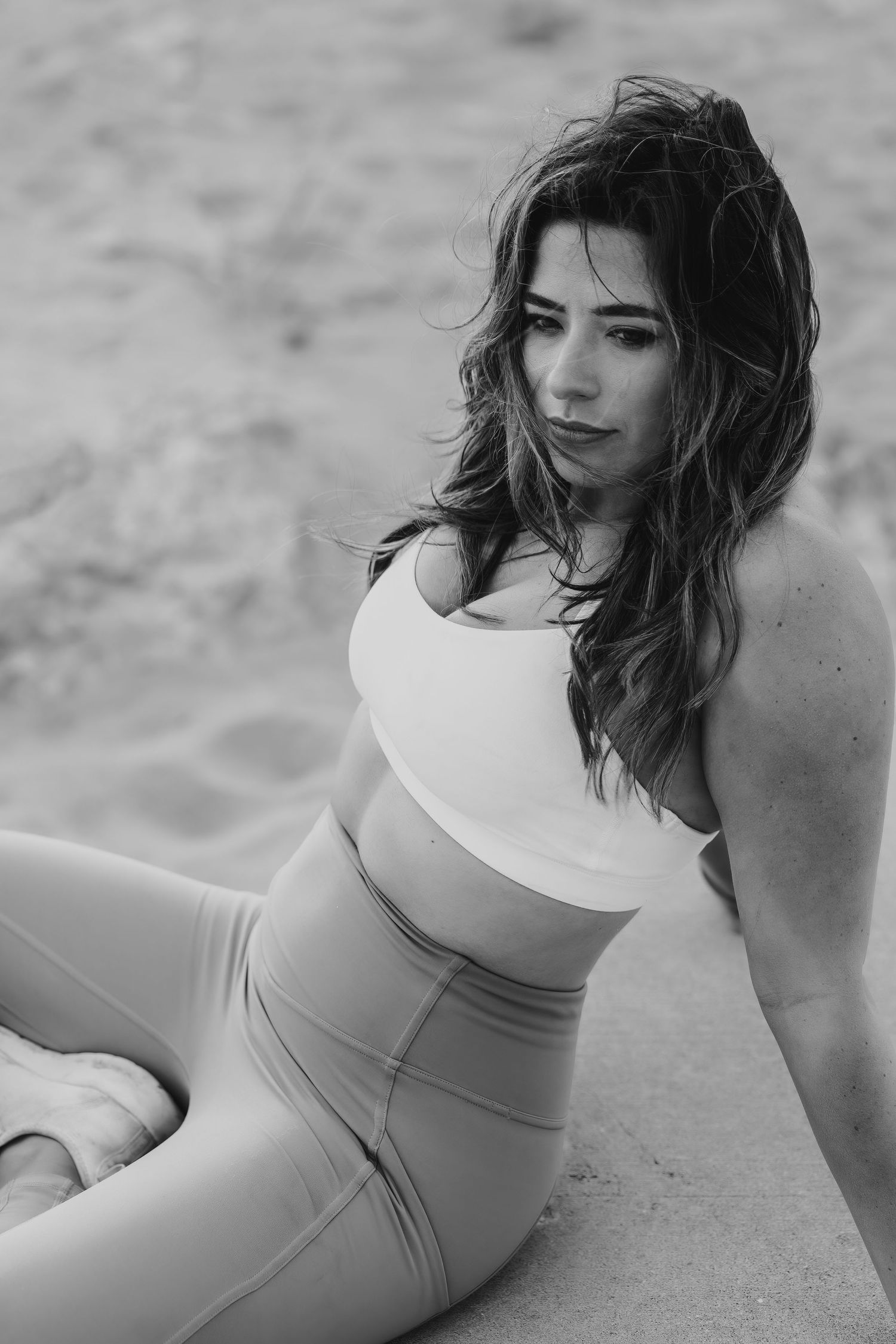 Fitness model in black and white wearing white crop top and leggings poses on beach.