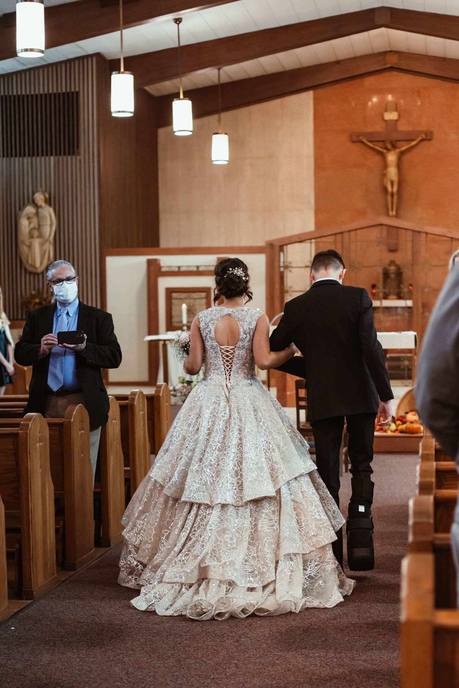 A stunning layered ball gown wedding dress with intricate lace details photographed from behind in a church.